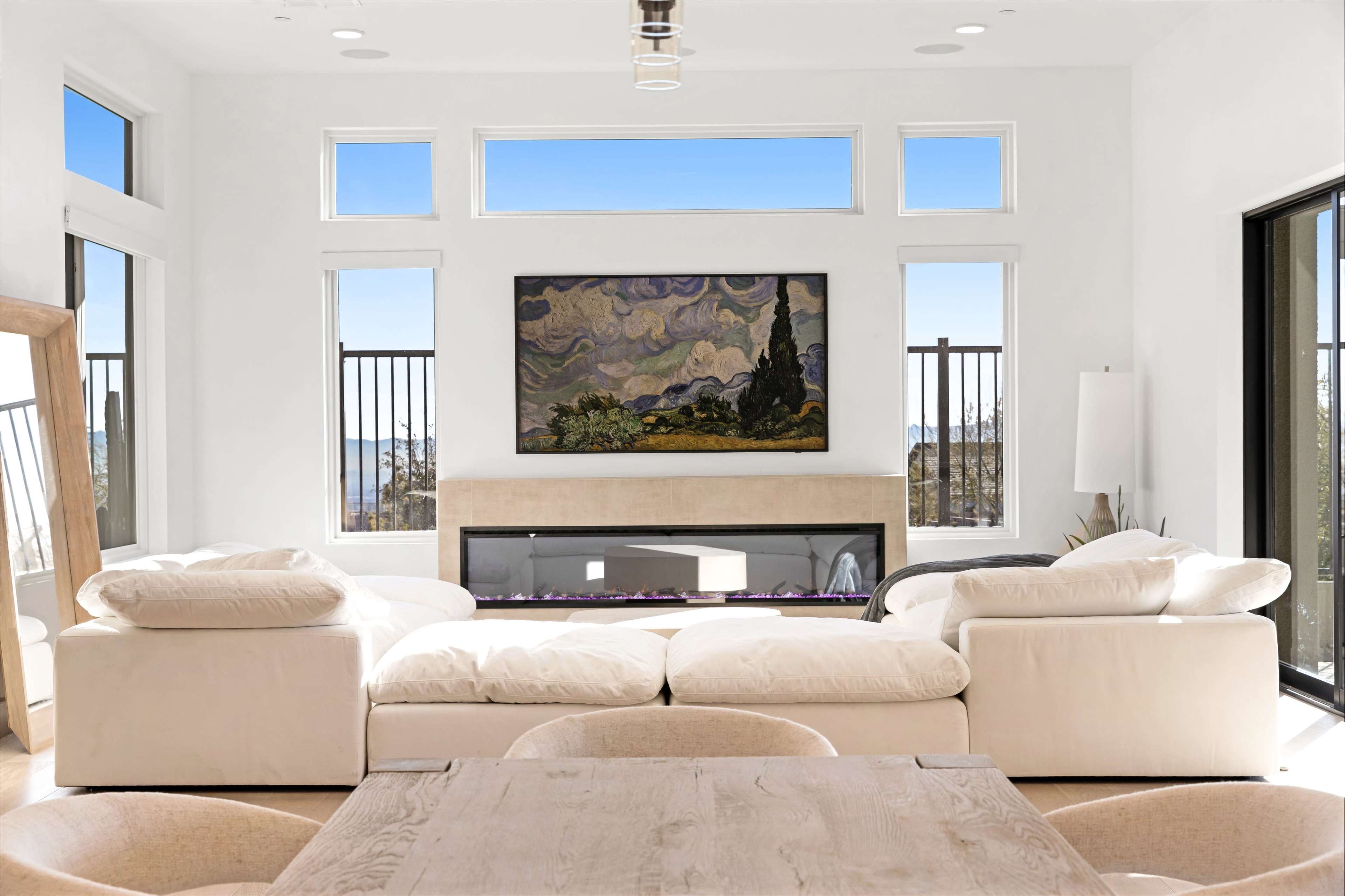 A modern living room with a large white sectional sofa facing a fireplace and a painting hung on the wall.