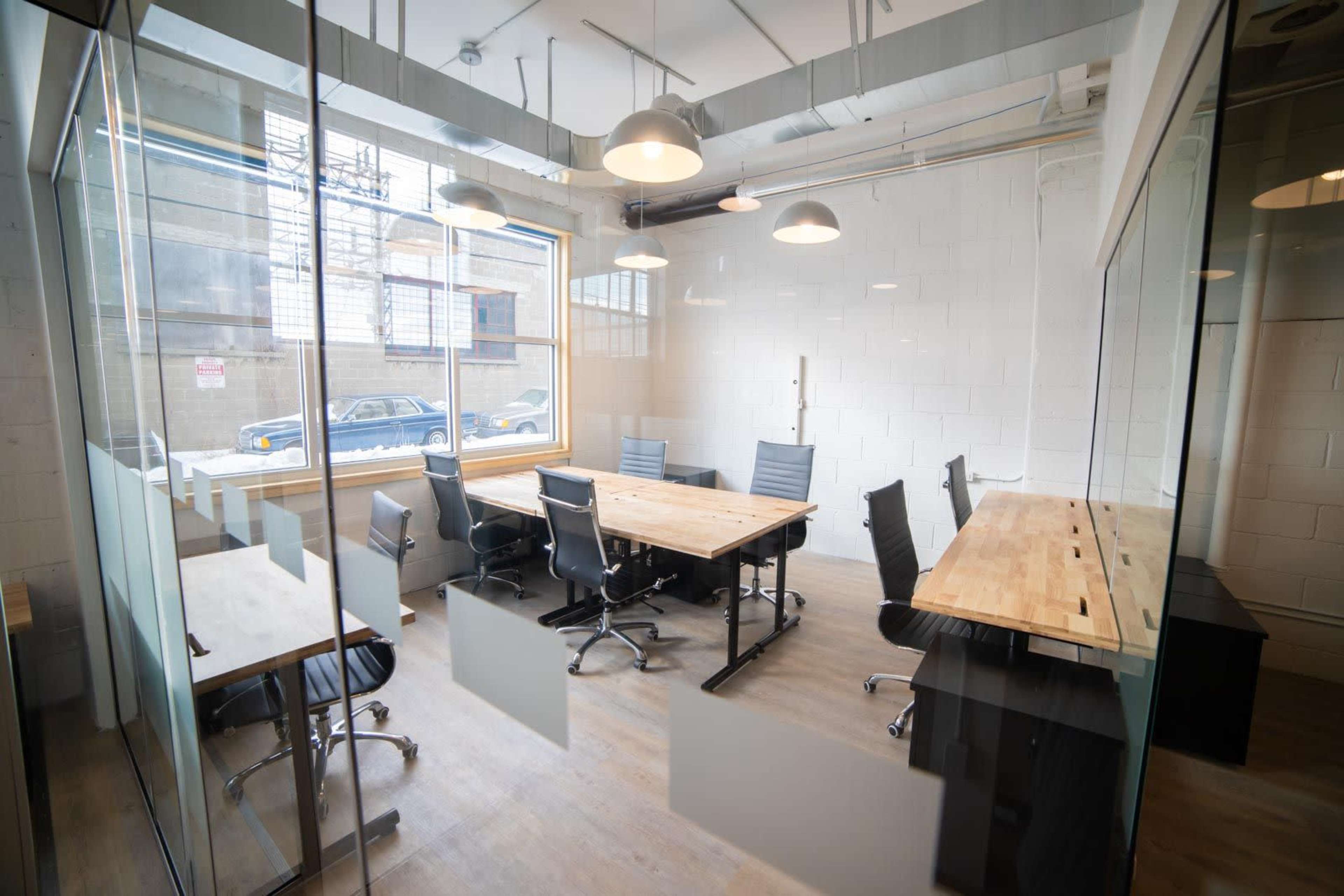 A conference room features a wooden table surrounded by black chairs and large windows, allowing natural light to enter.