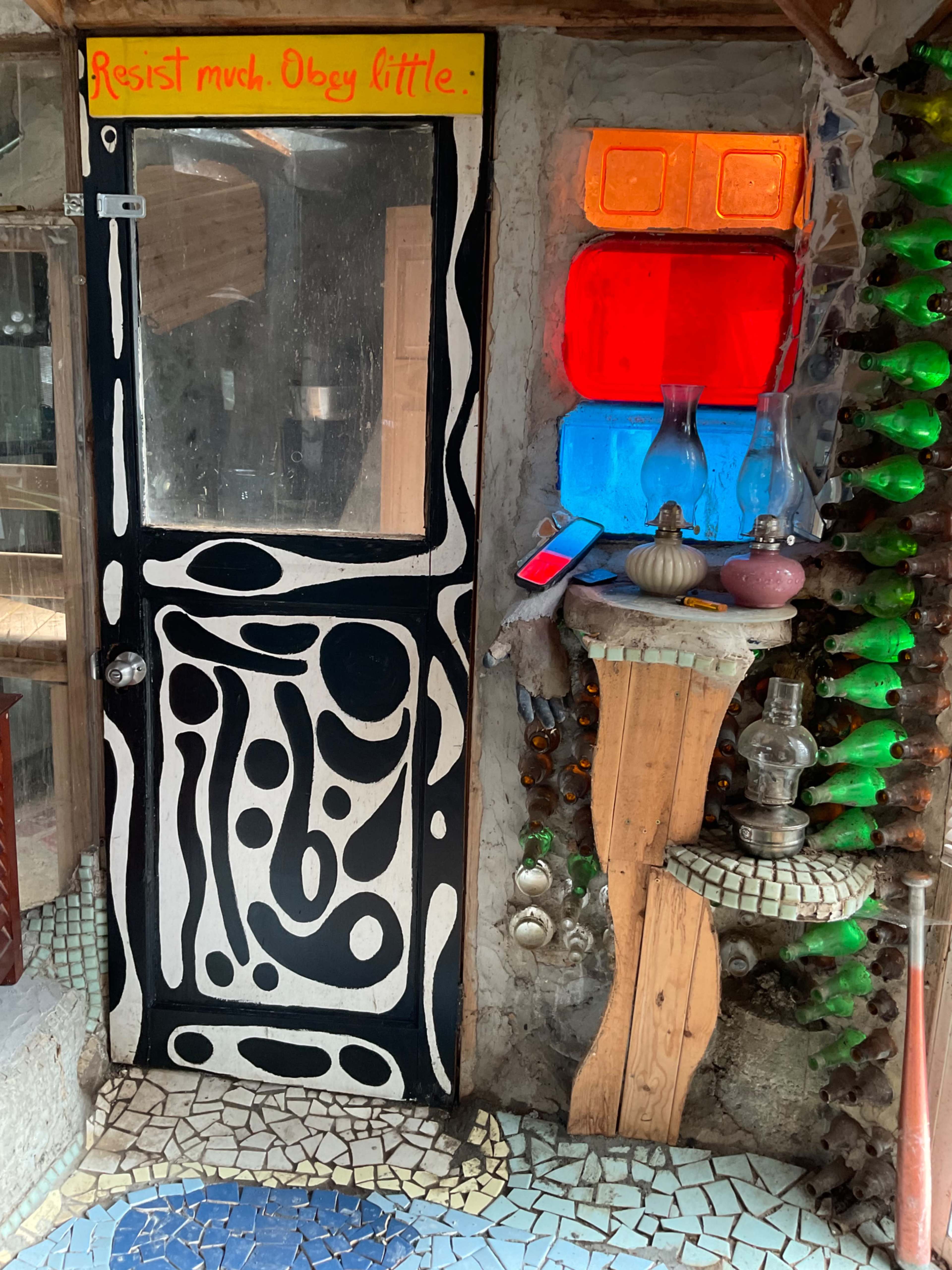 A uniquely decorated door with abstract patterns, next to a table with decorative artifacts and colorful glass panes.
