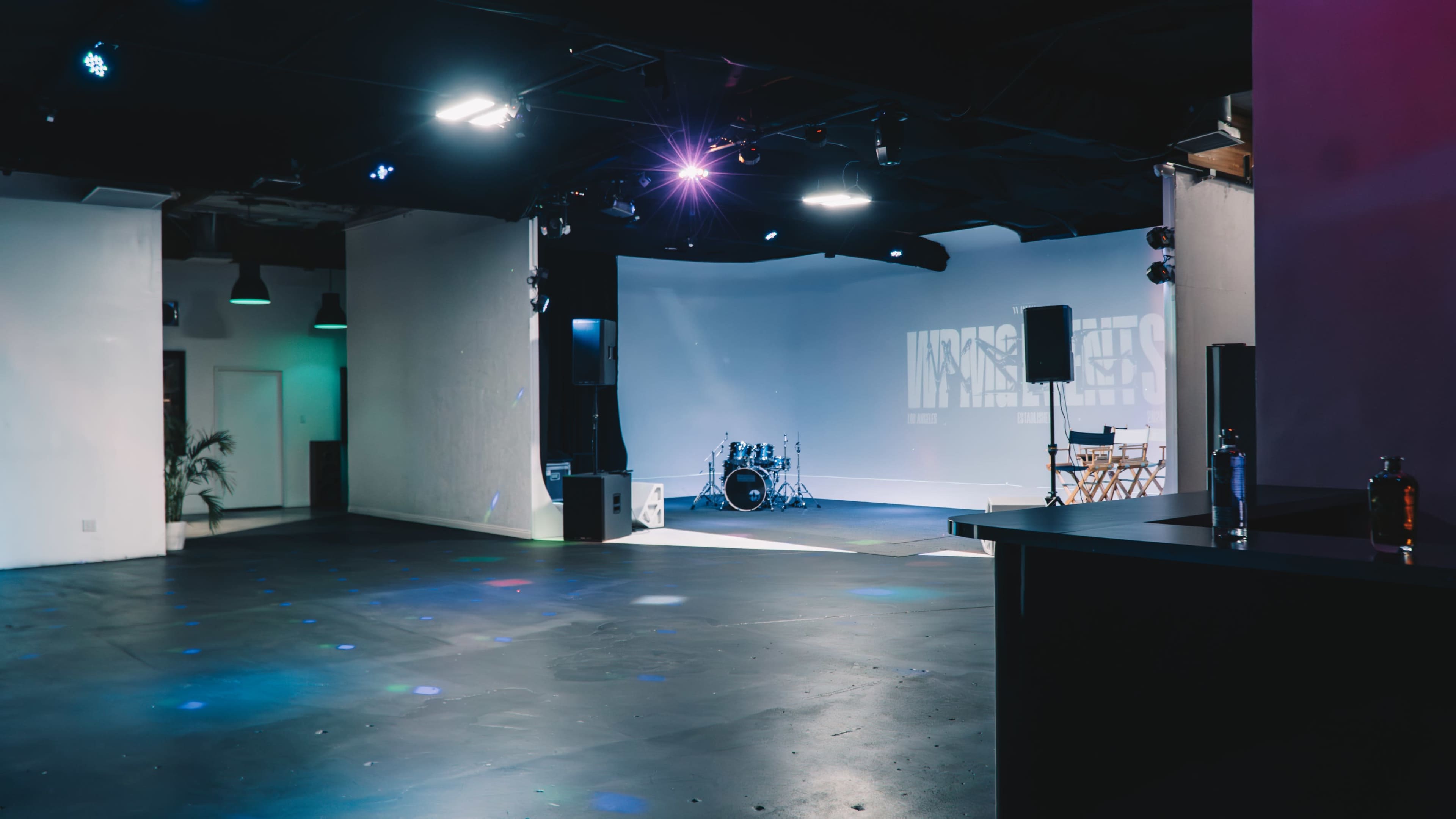A spacious performance venue with a stage, drum set, and dim lighting.