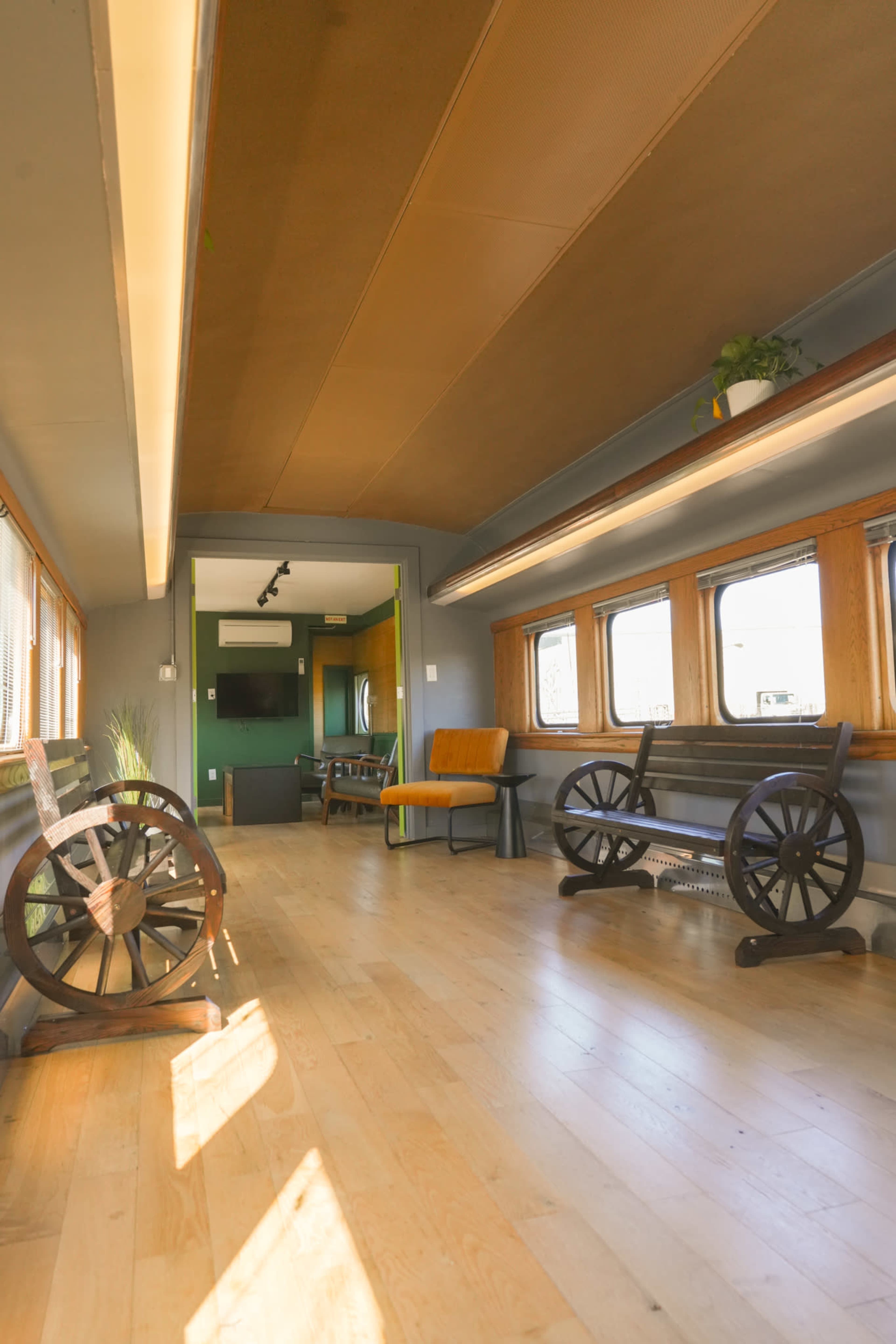 The interior of a vintage train car features wooden floors, large windows, and a seating area with rustic decor.