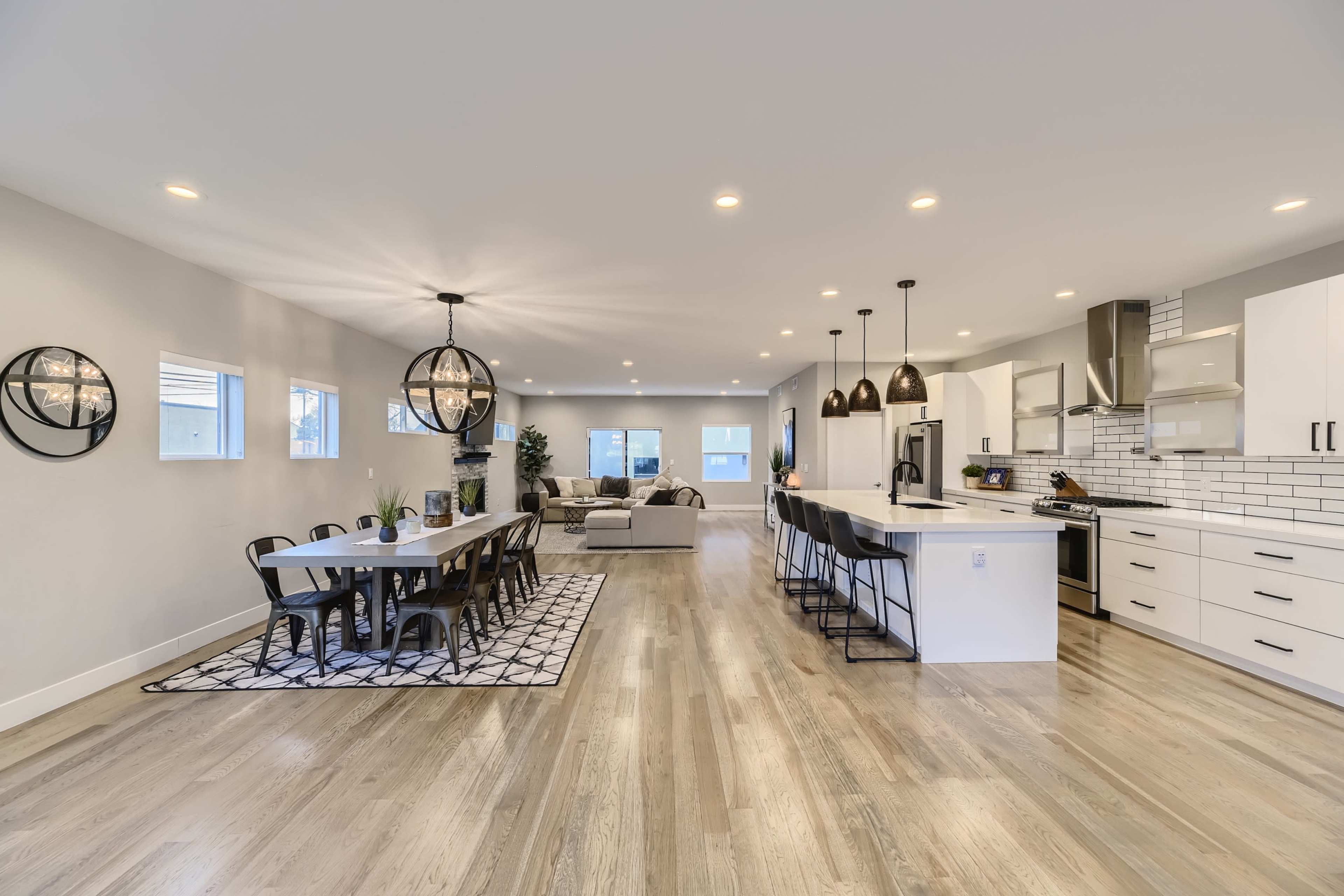 A spacious modern kitchen and dining area with a long table, black chairs, and a living room in the background.