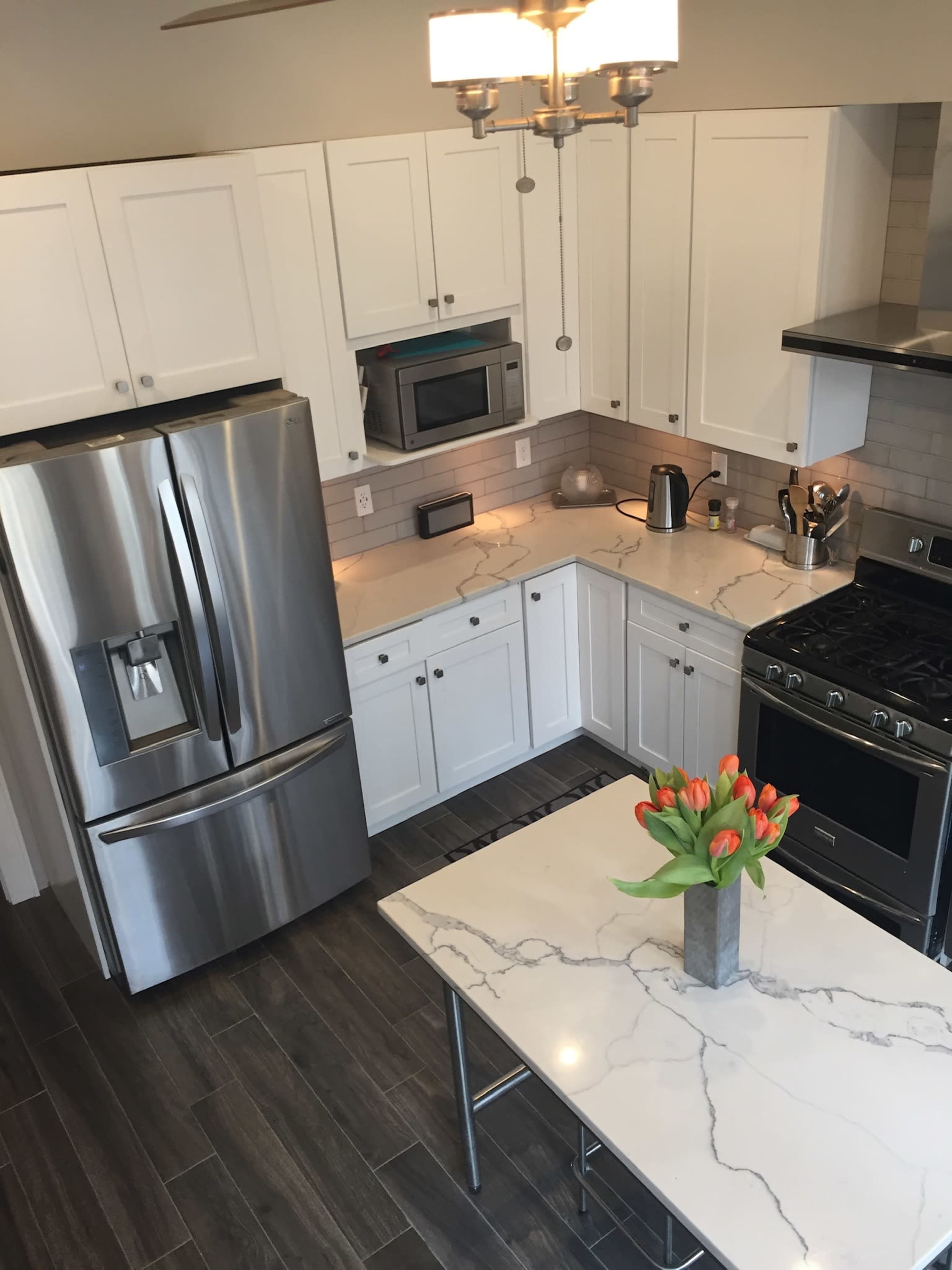 A modern kitchen features white cabinetry, stainless steel appliances, and a central island topped with a marble surface and a vase of tulips.