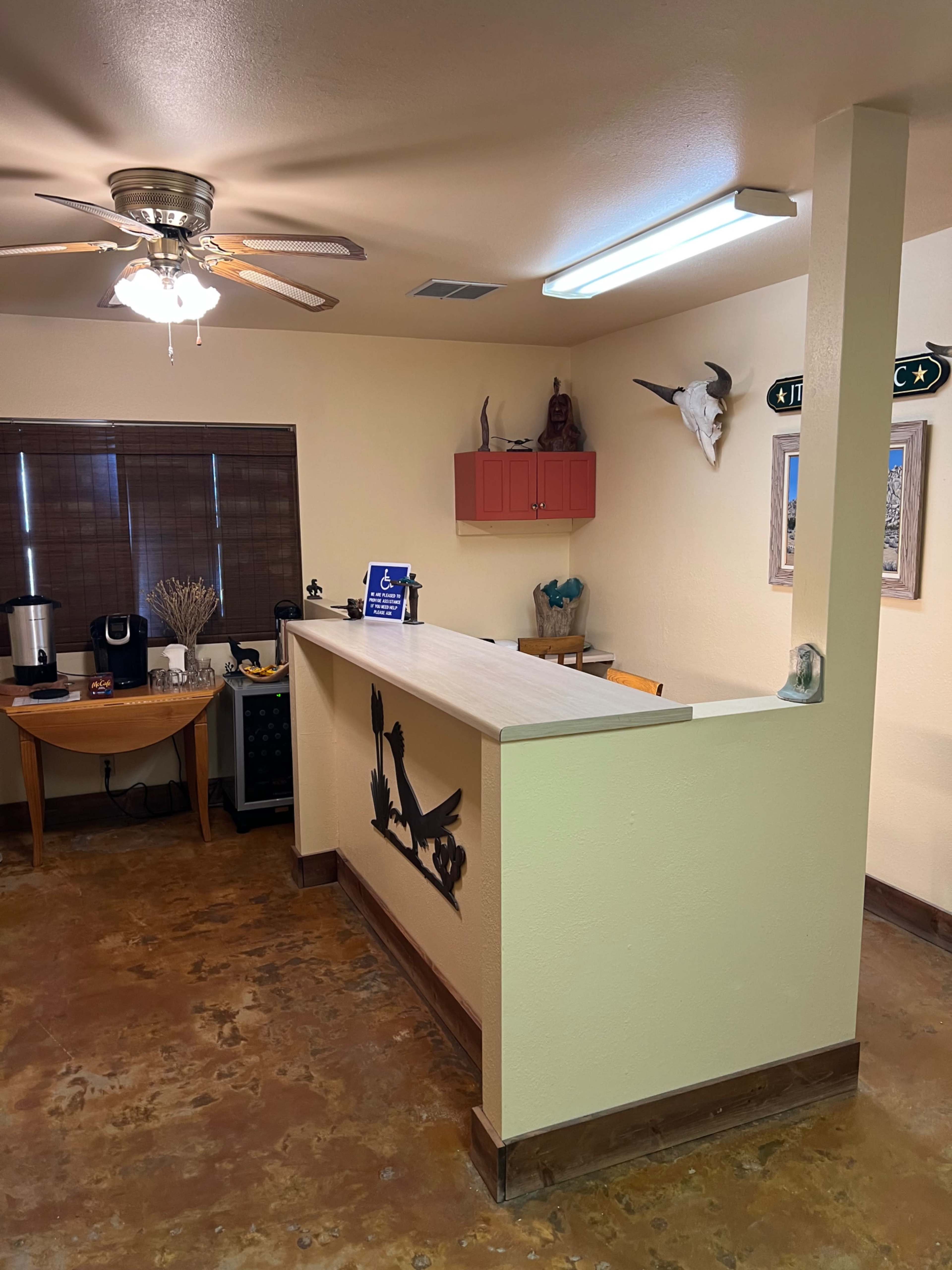 The image shows a light-colored interior with a reception area featuring a counter, a coffee maker, and decorative items on the walls.
