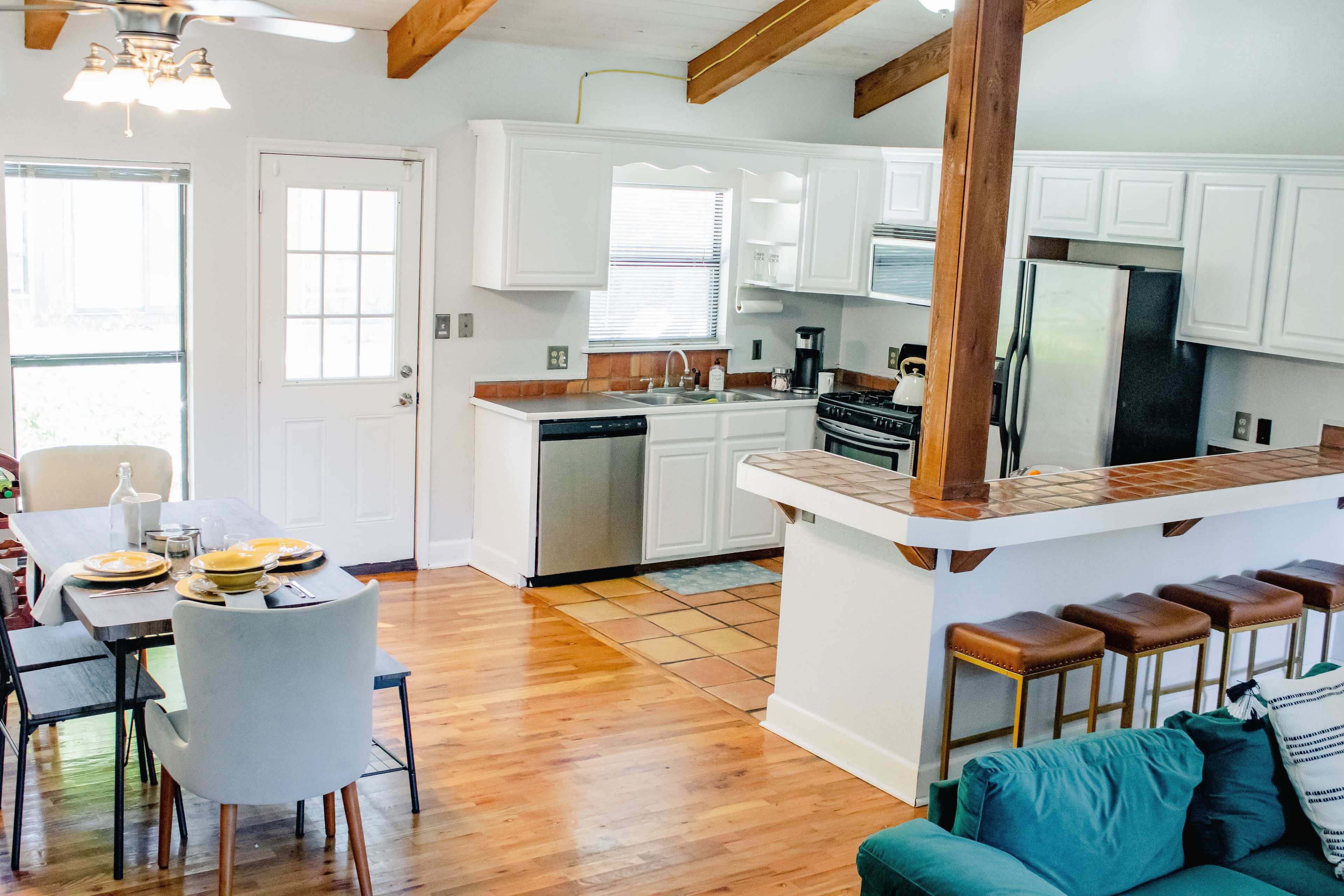 A modern kitchen and dining area with white cabinetry, stainless steel appliances, a dining table set for four, and a living space featuring a green couch.