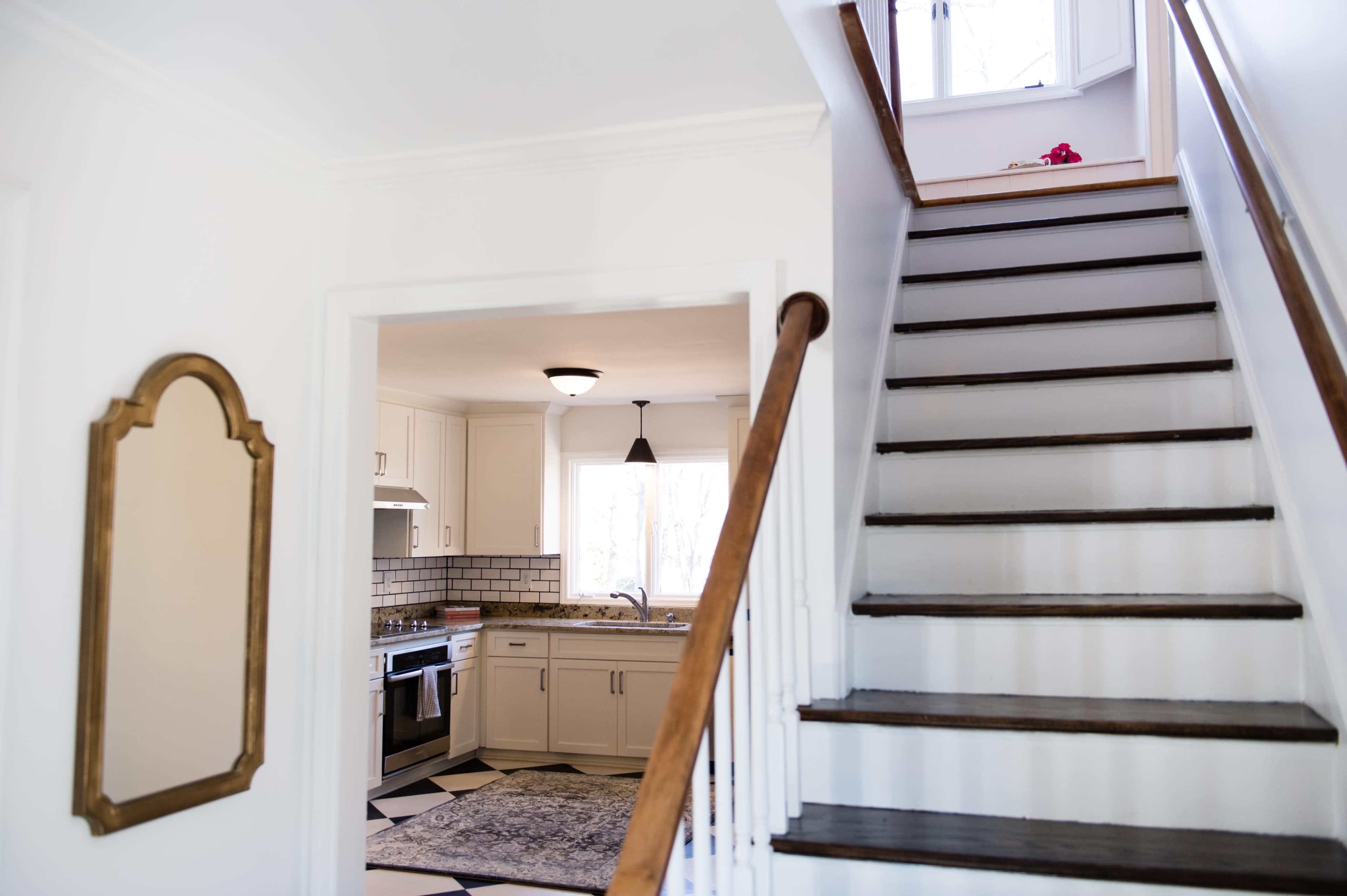 A well-lit home interior featuring a staircase leading to a second floor and an open kitchen visible through an archway.