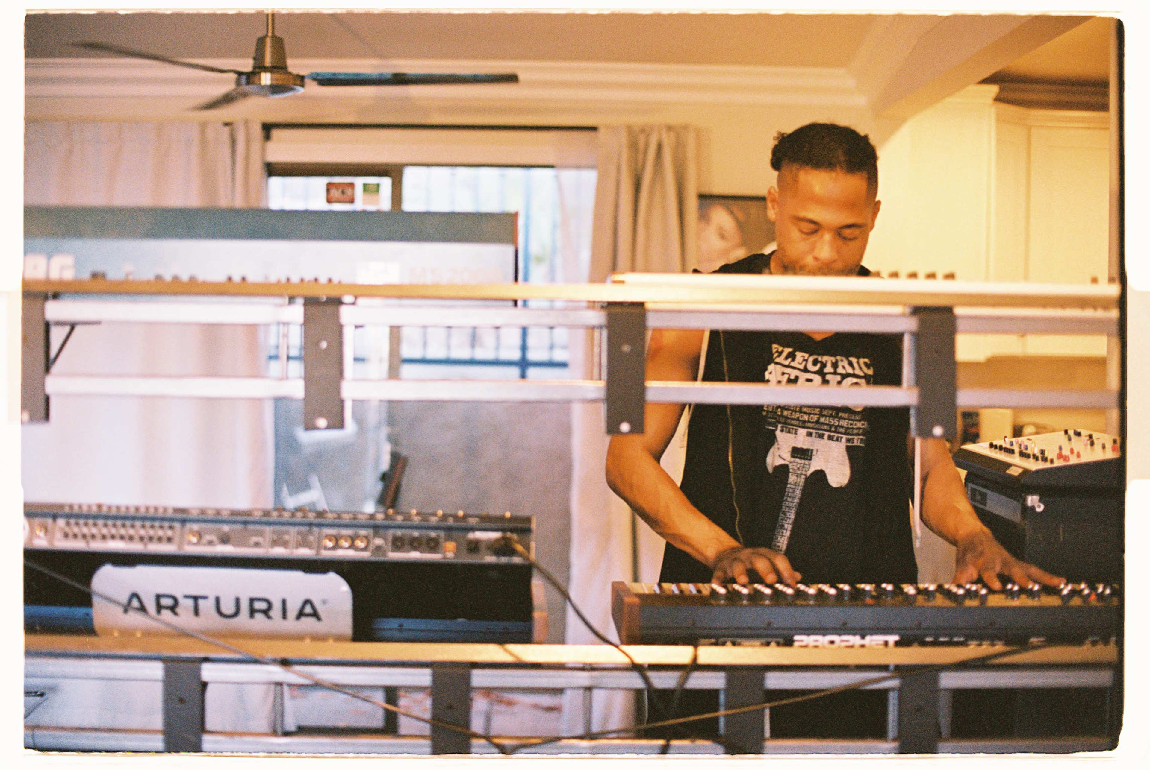 A musician plays a keyboard in a room filled with electronic music equipment.
