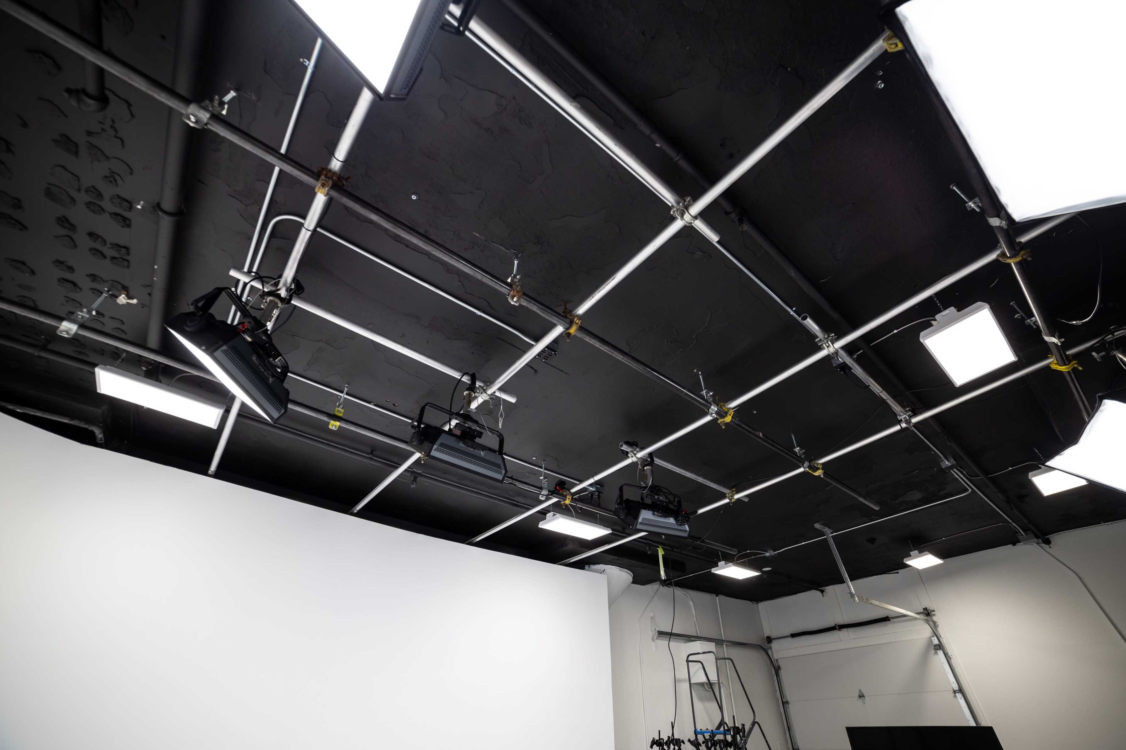A studio ceiling with overhead lighting fixtures and a blank white backdrop in a production space.