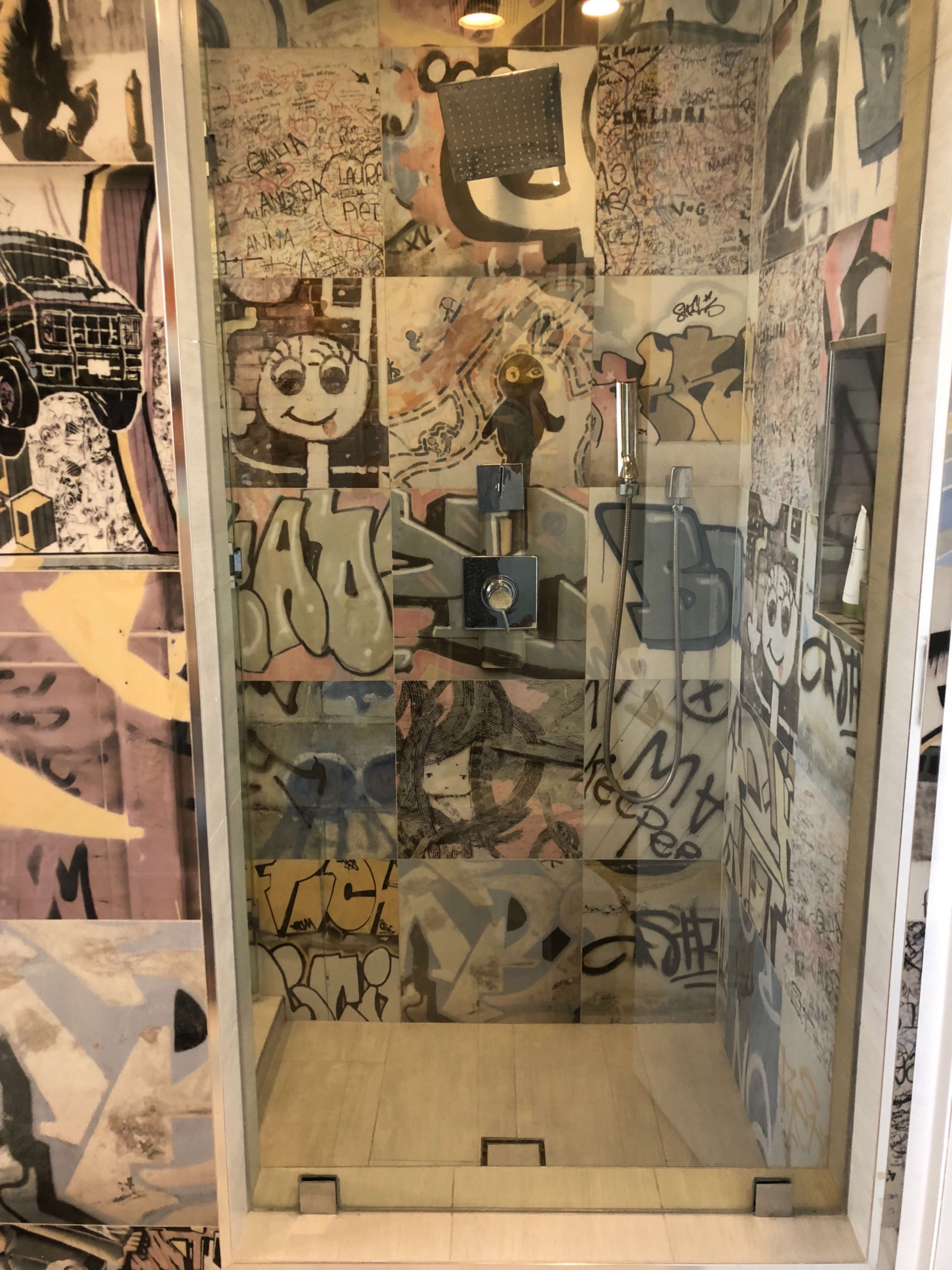 A glass shower enclosure surrounded by walls covered in colorful graffiti and street art.