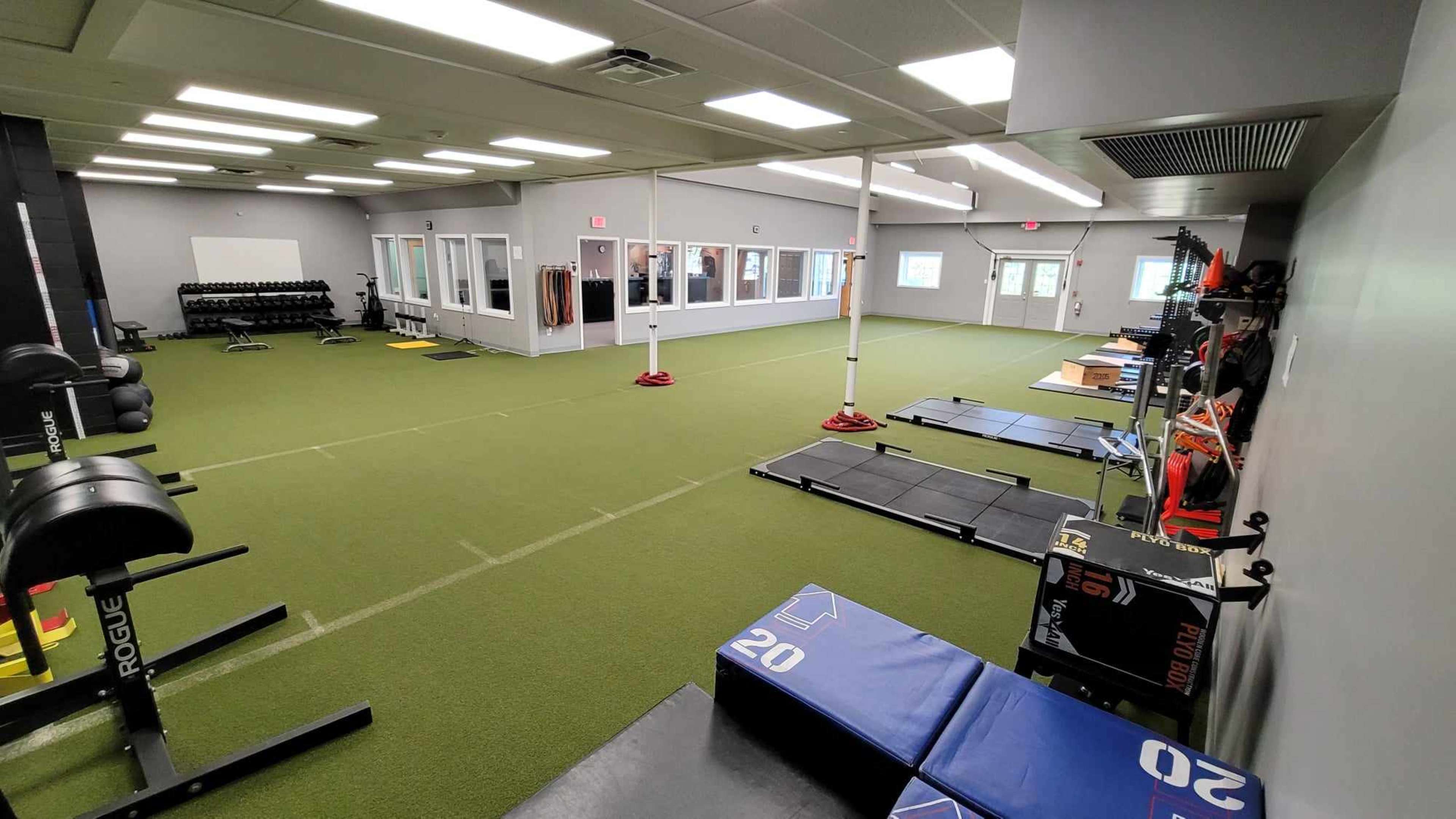 A spacious indoor training facility featuring workout equipment, exercise mats, and artificial turf.