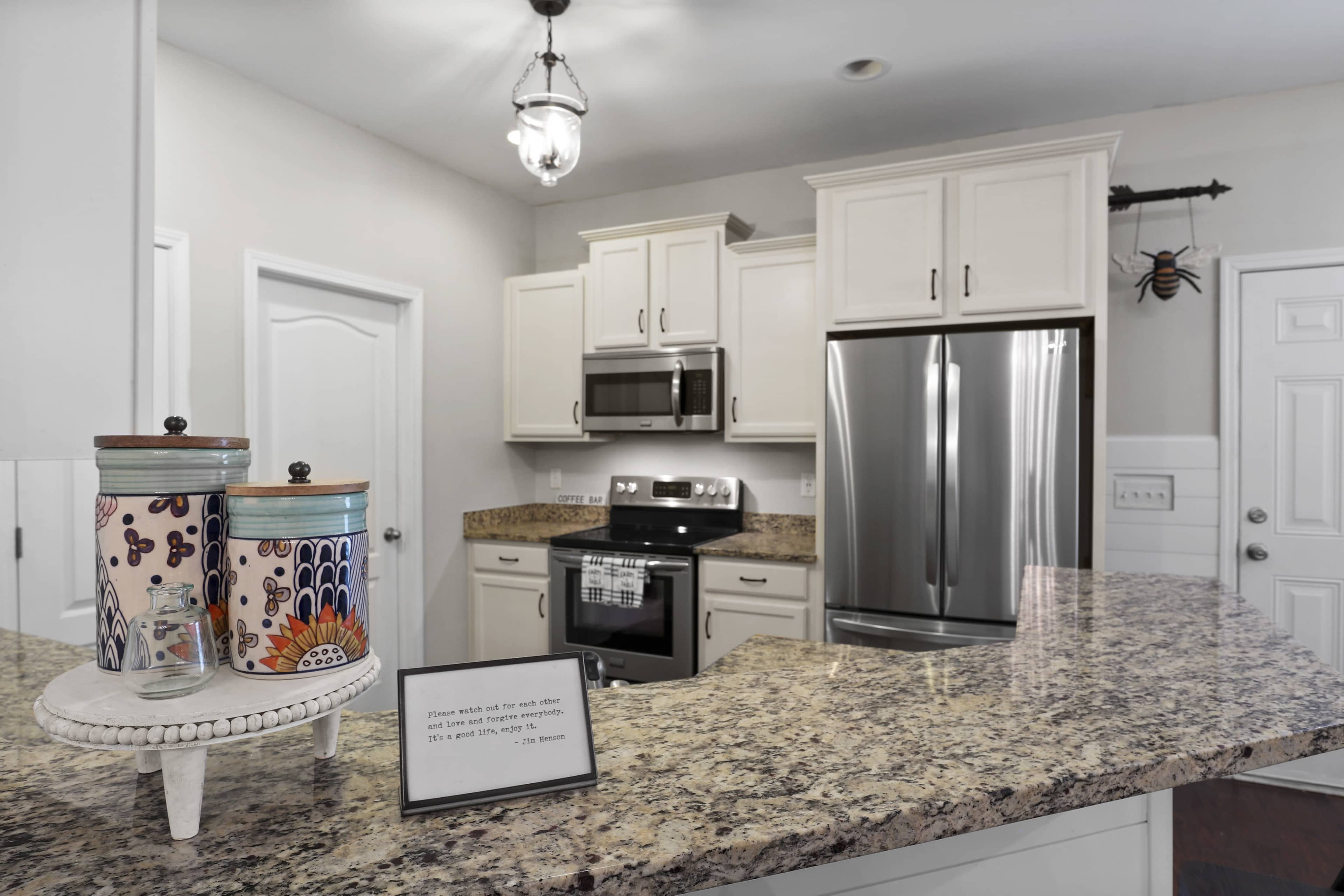 A modern kitchen features white cabinetry, granite countertops, stainless steel appliances, and decorative storage containers on a circular tray.