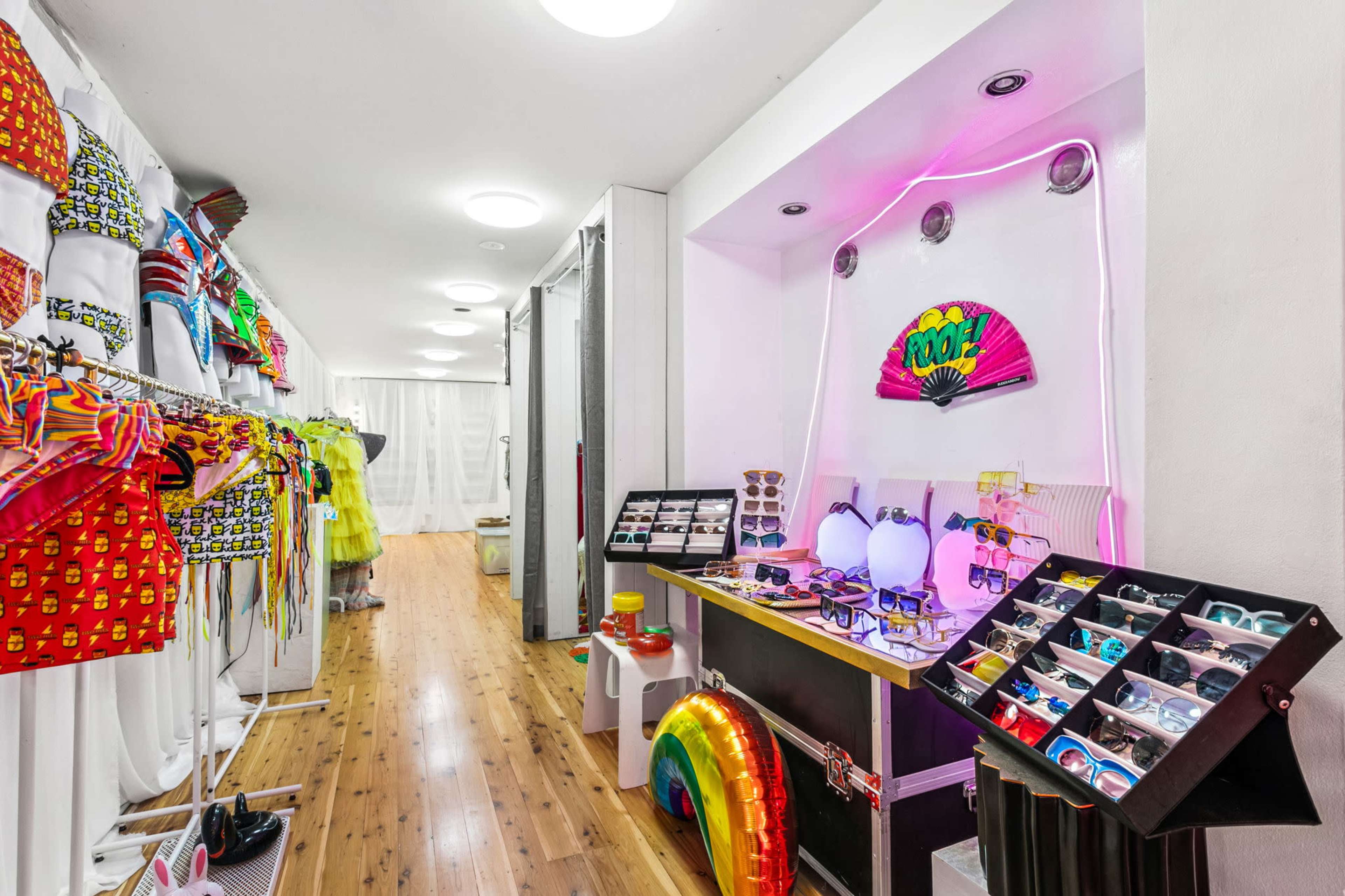 The image shows a boutique interior with colorful clothing displays and various sunglasses arranged on black stands.