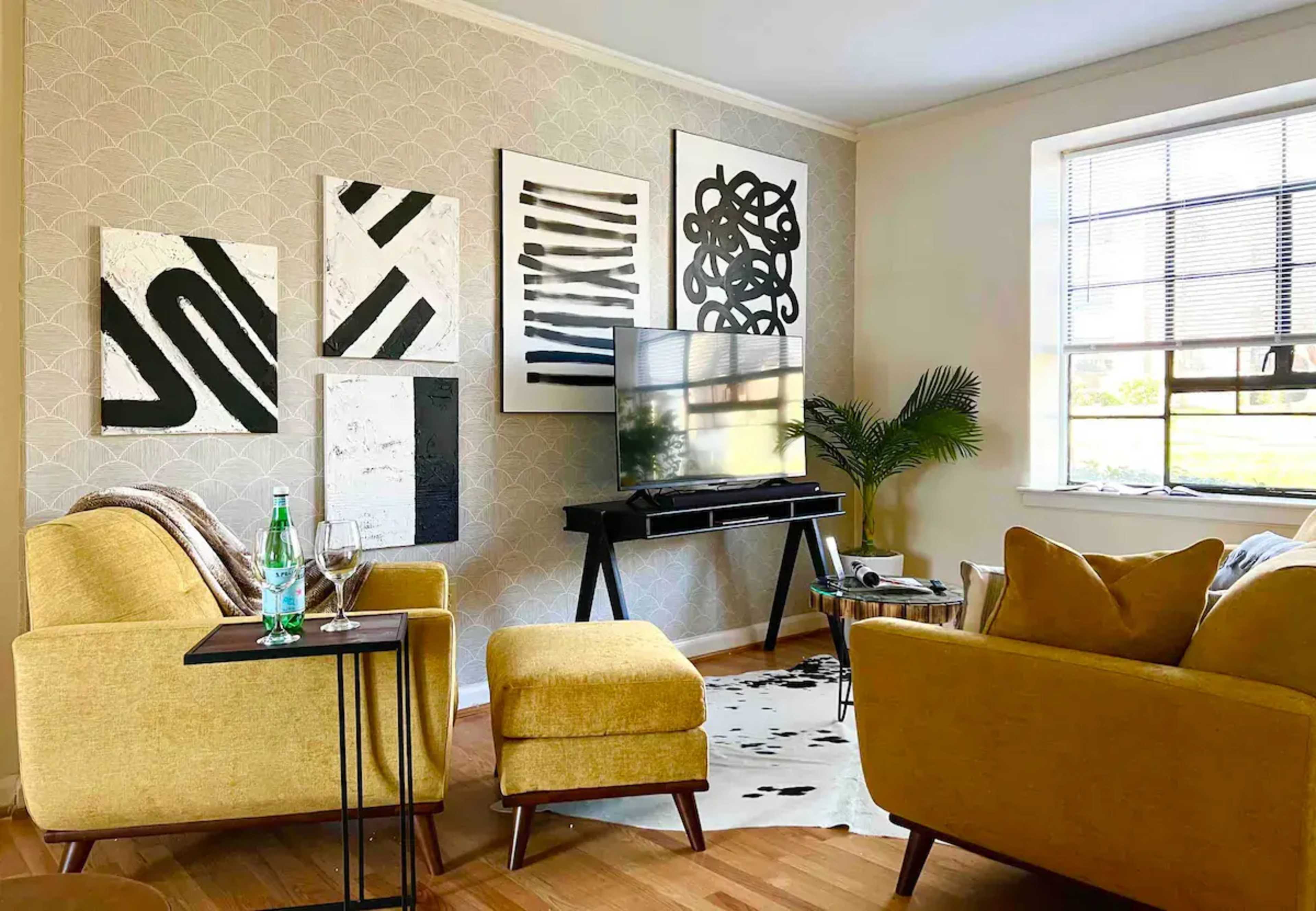 A modern living room featuring yellow furniture, black and white abstract wall art, and a television on a sleek stand.