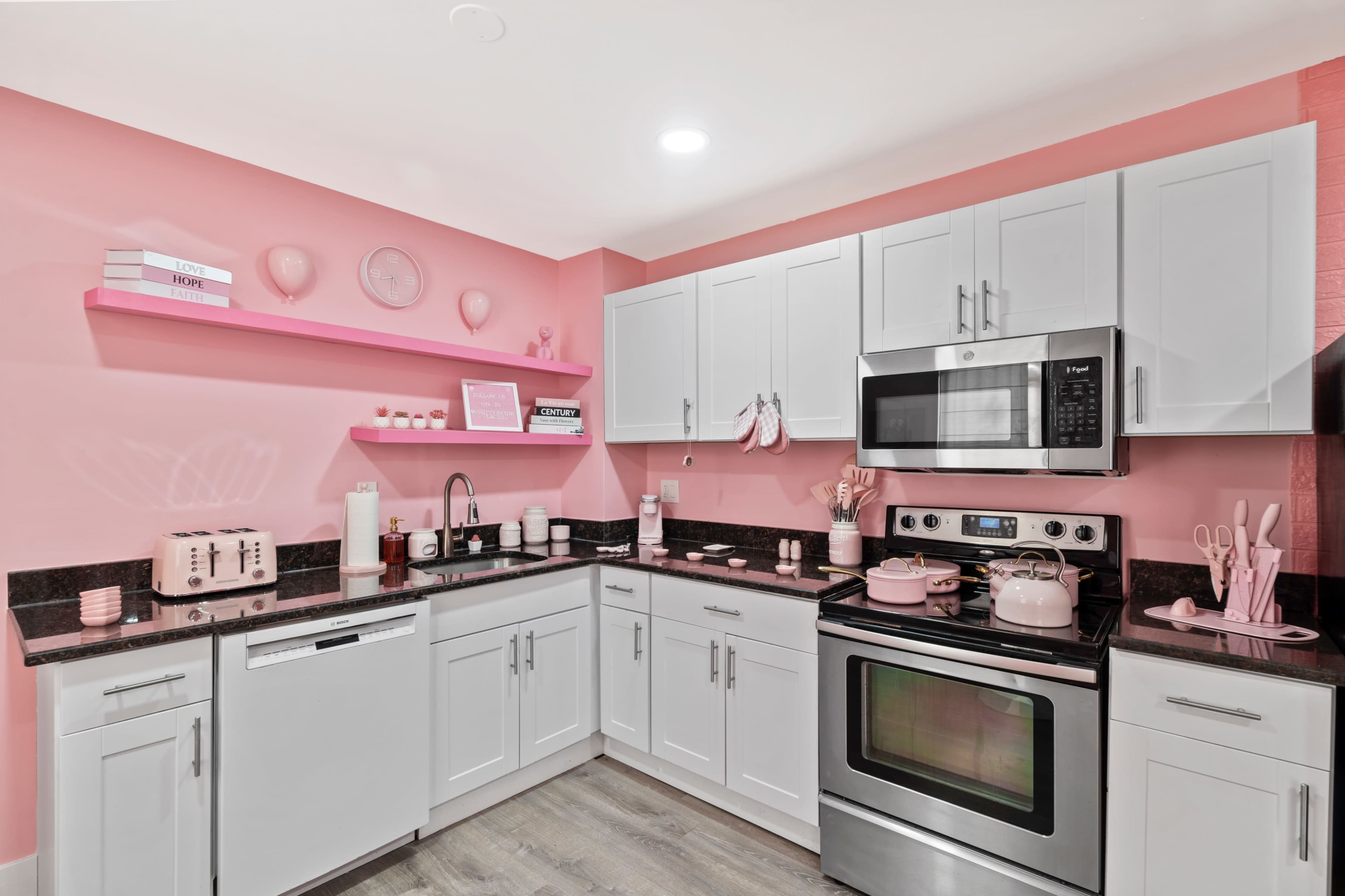 The kitchen features pink walls, white cabinetry, and black countertops with kitchen appliances and decor in coordinating colors.