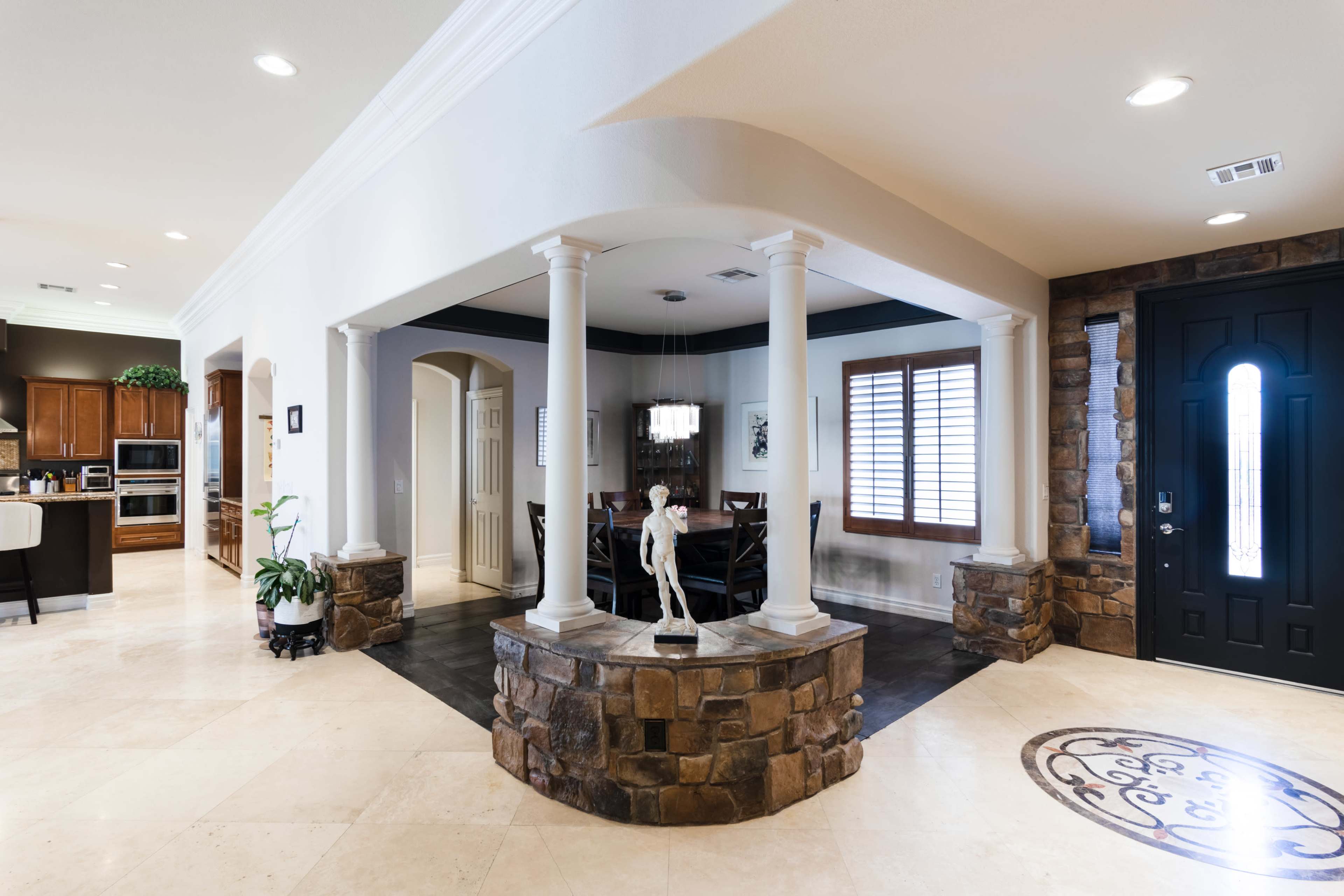 A spacious foyer with arched columns and a stone base, leading to a kitchen and dining area.