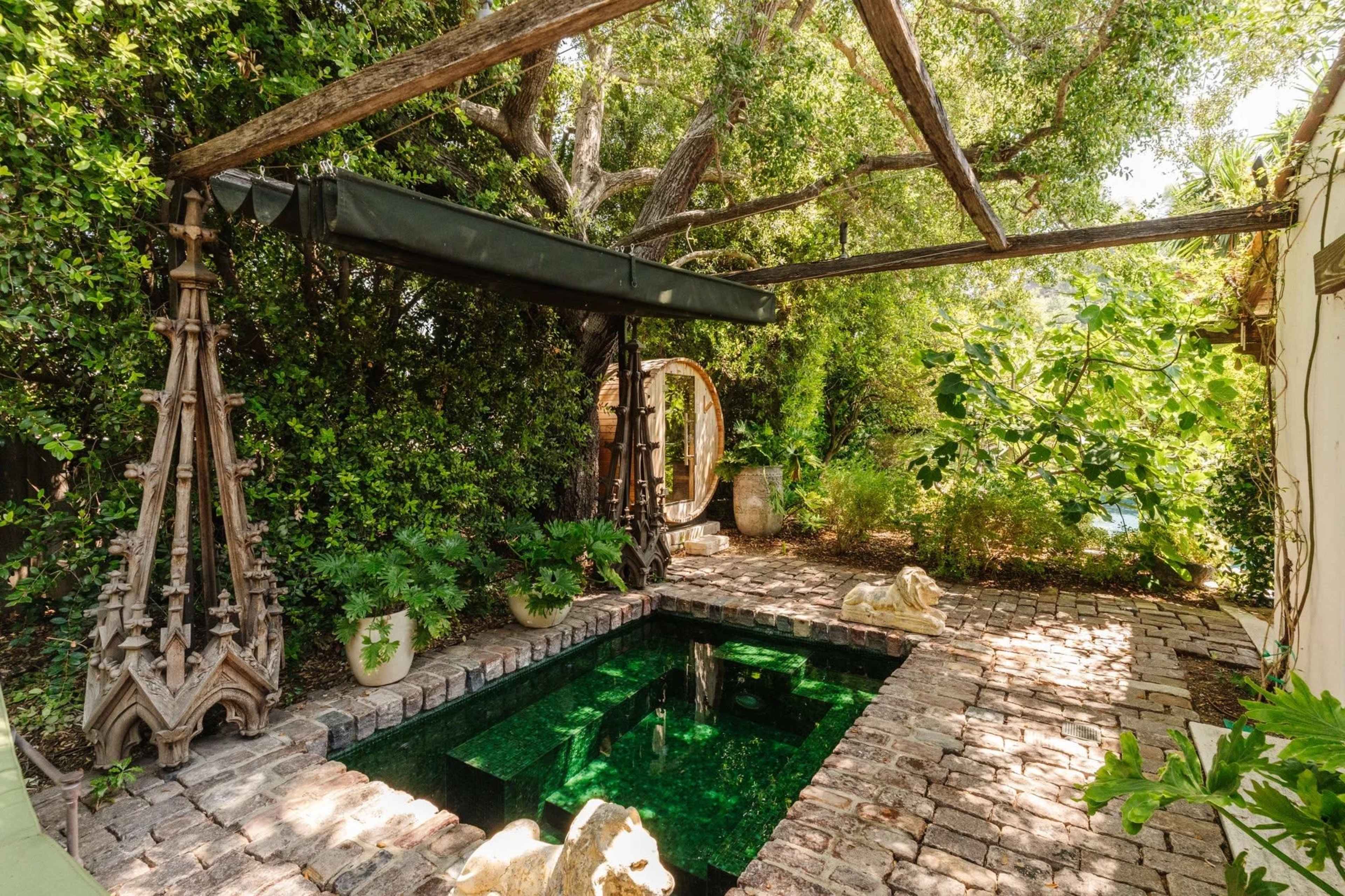 The image shows a secluded outdoor area featuring a rectangular green pool surrounded by stone flooring and lush vegetation.