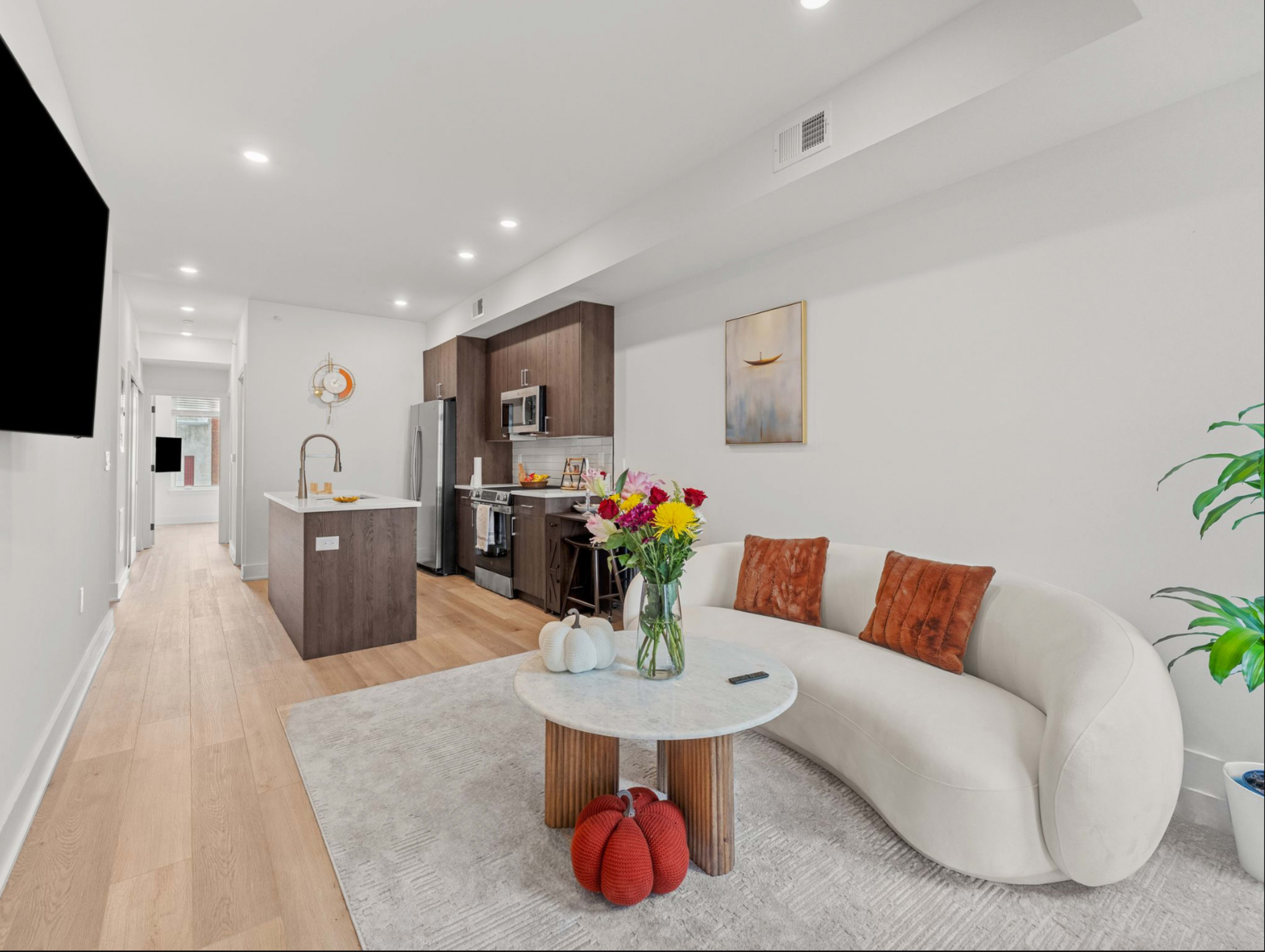 A modern living space features a curved sofa, a circular table, and a stylish kitchen with stainless steel appliances.