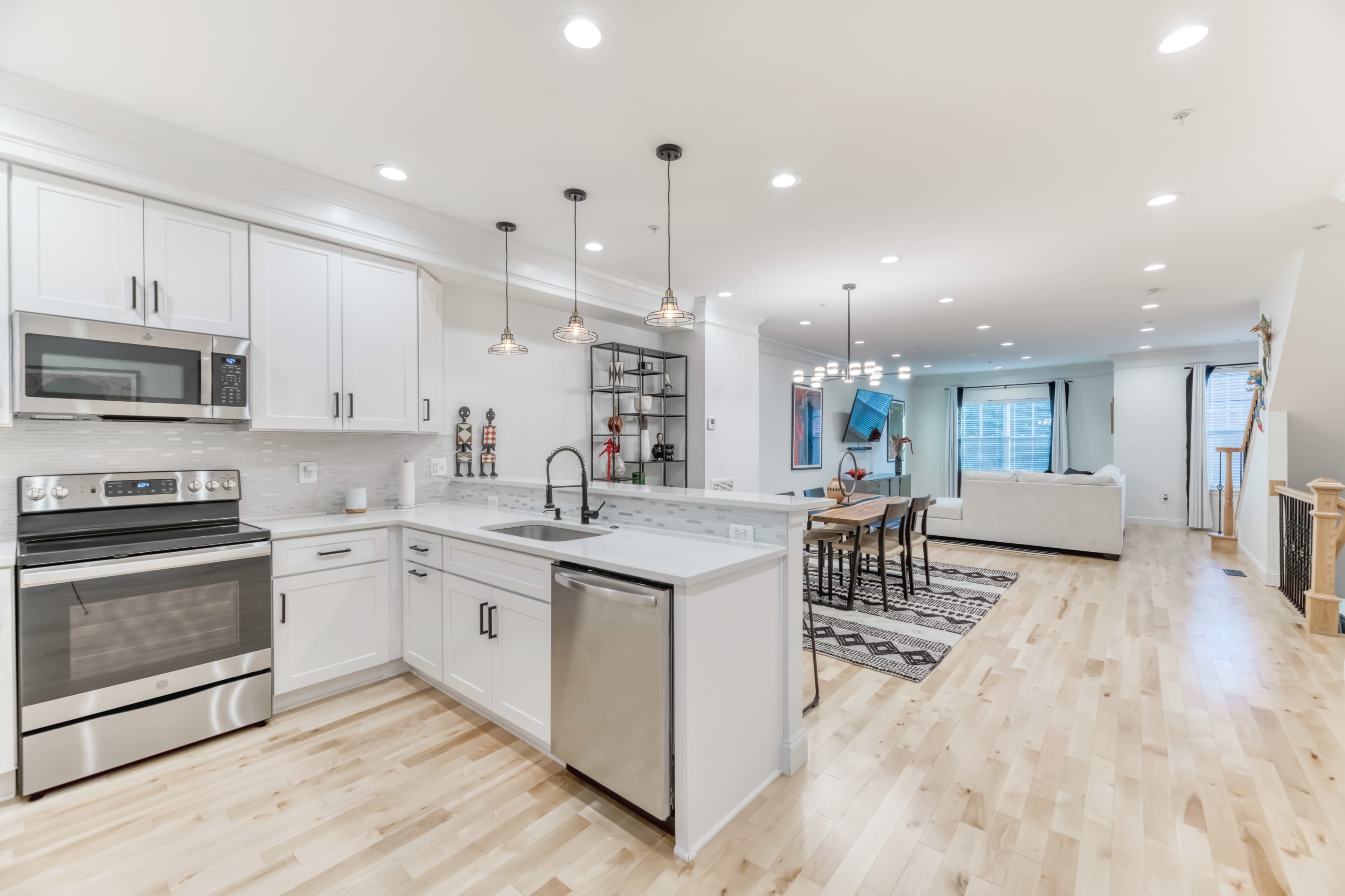 A modern kitchen with white cabinetry, stainless steel appliances, and a large island, leading into an open-concept living area.