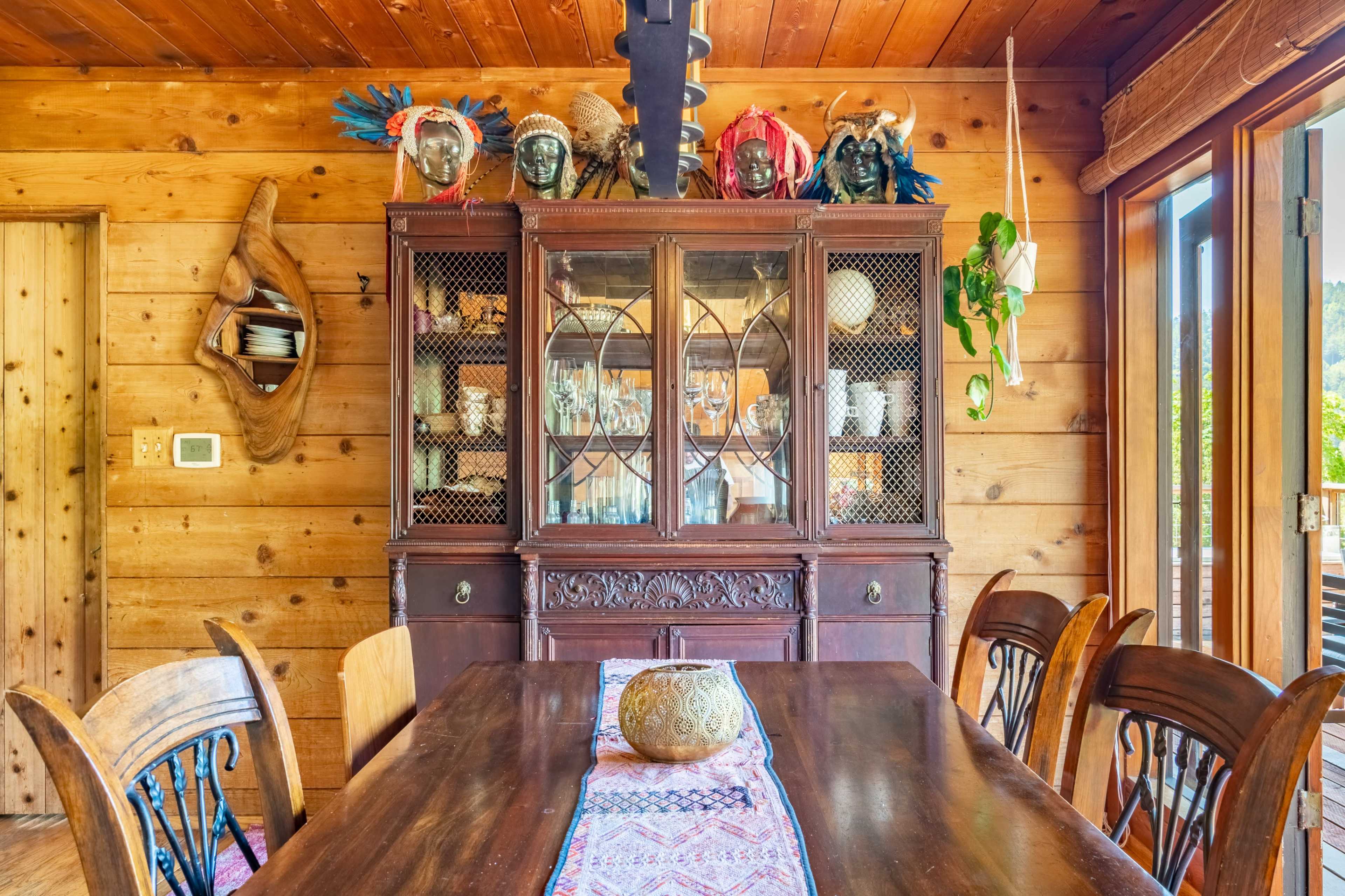 A wooden dining area featuring a large table, a decorative hutch filled with dishes, and various ornamental items displayed on top of the hutch.