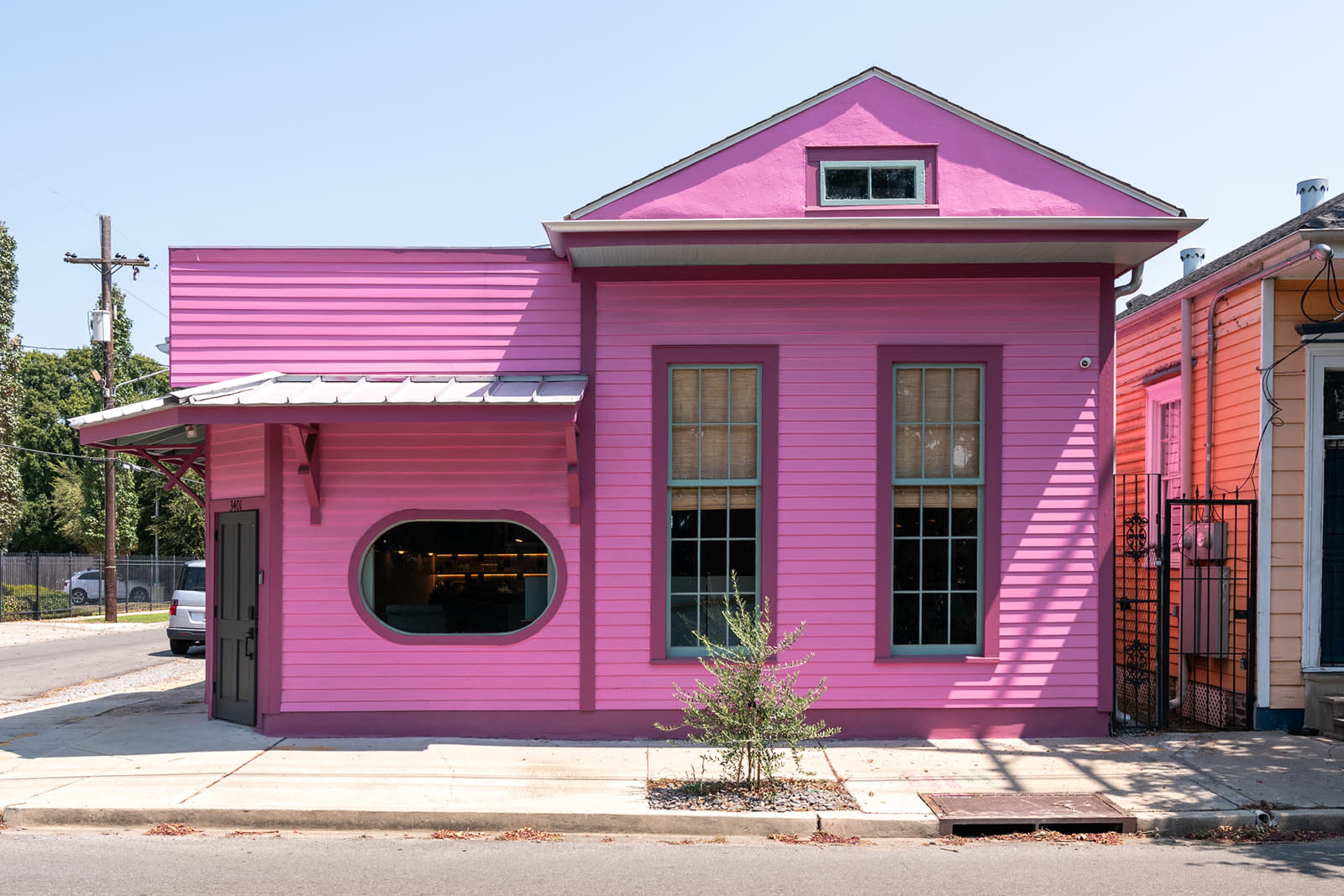 A brightly colored pink building with large windows stands on a street corner.