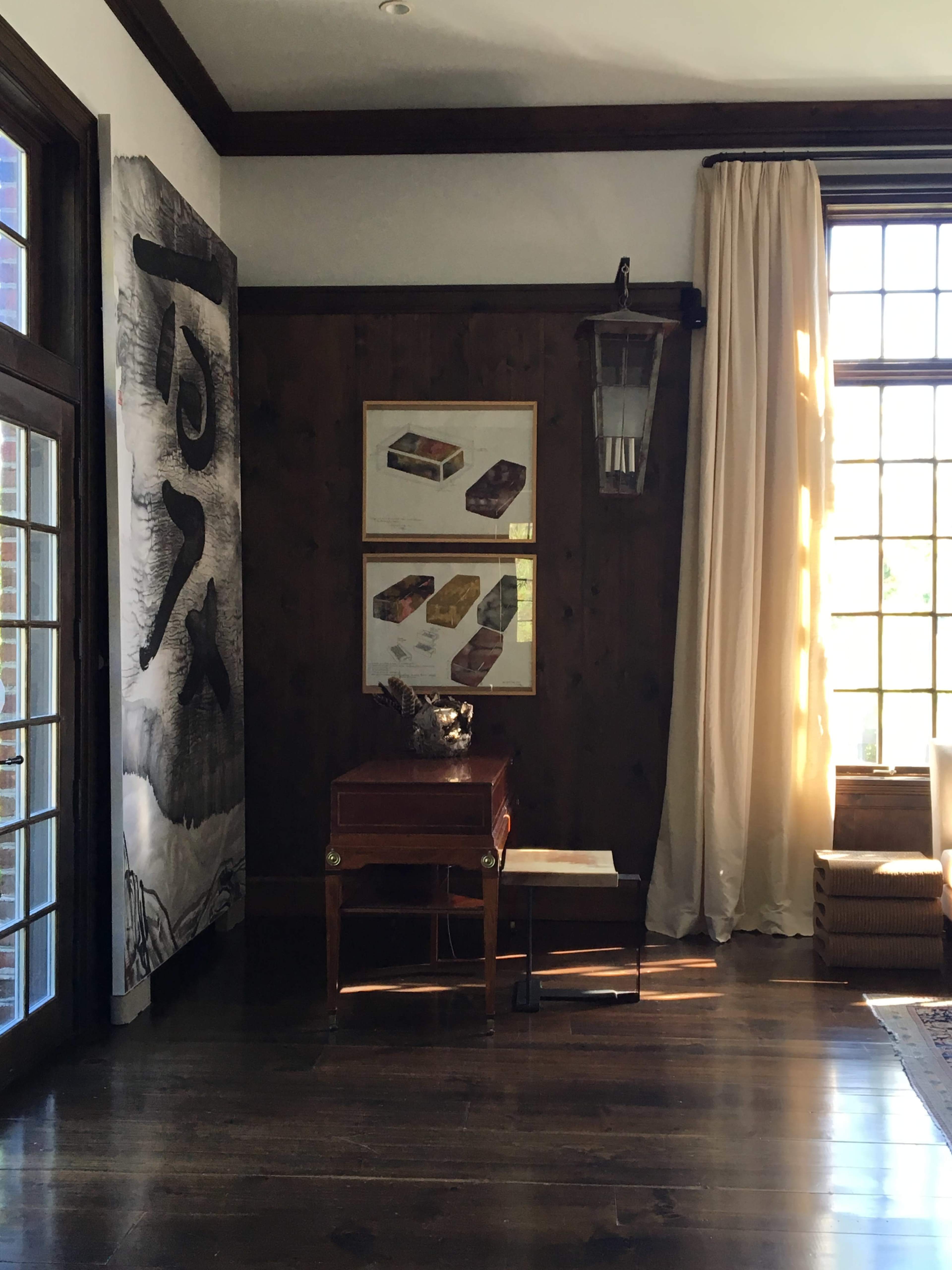 A well-lit interior space featuring a wooden wall, a table with a decorative item, and framed artwork displaying various boxes on the adjacent wall.