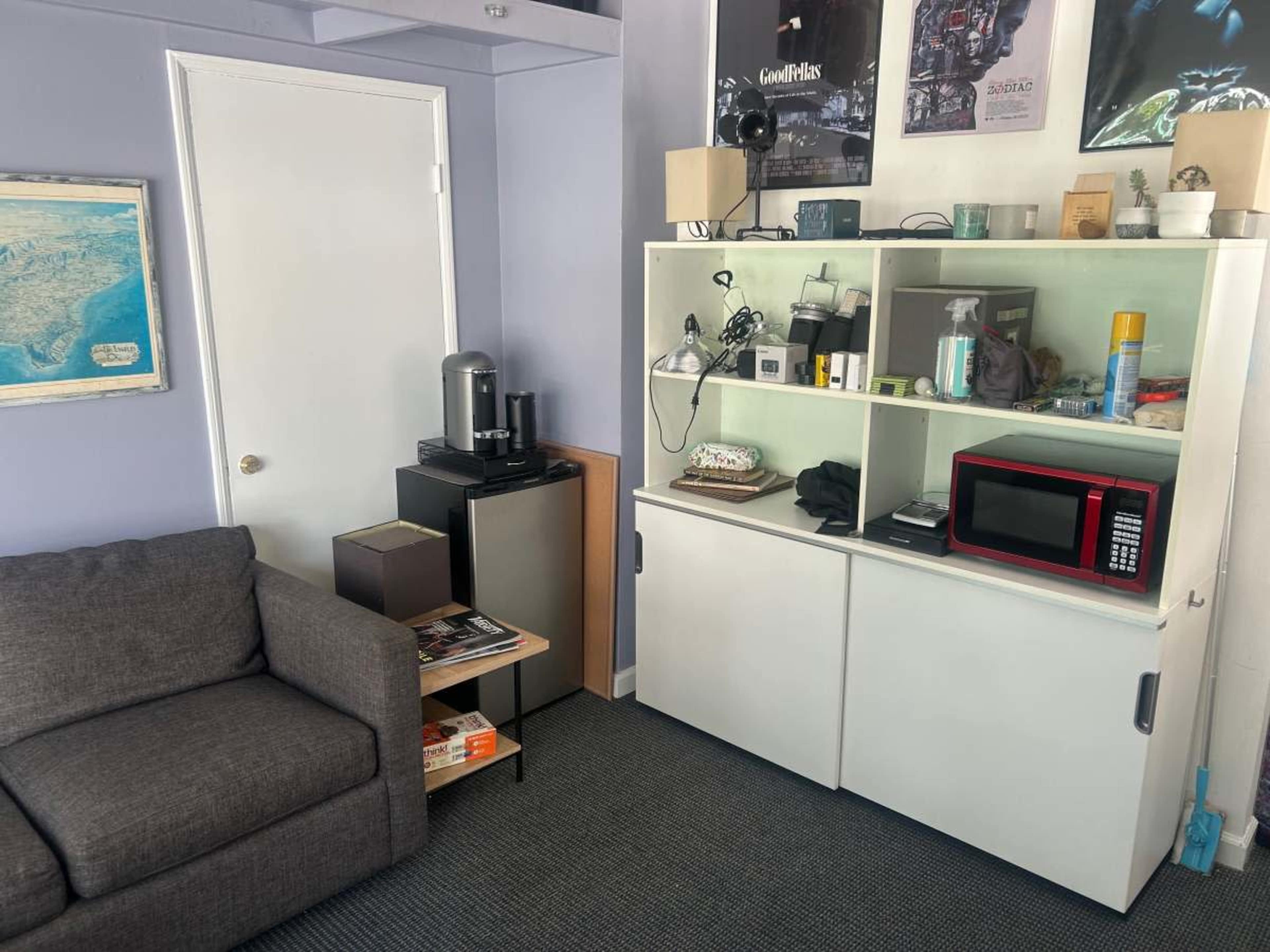 The image shows a small living space with a gray sofa, a white cabinet containing a microwave and various items, and a door in the background.