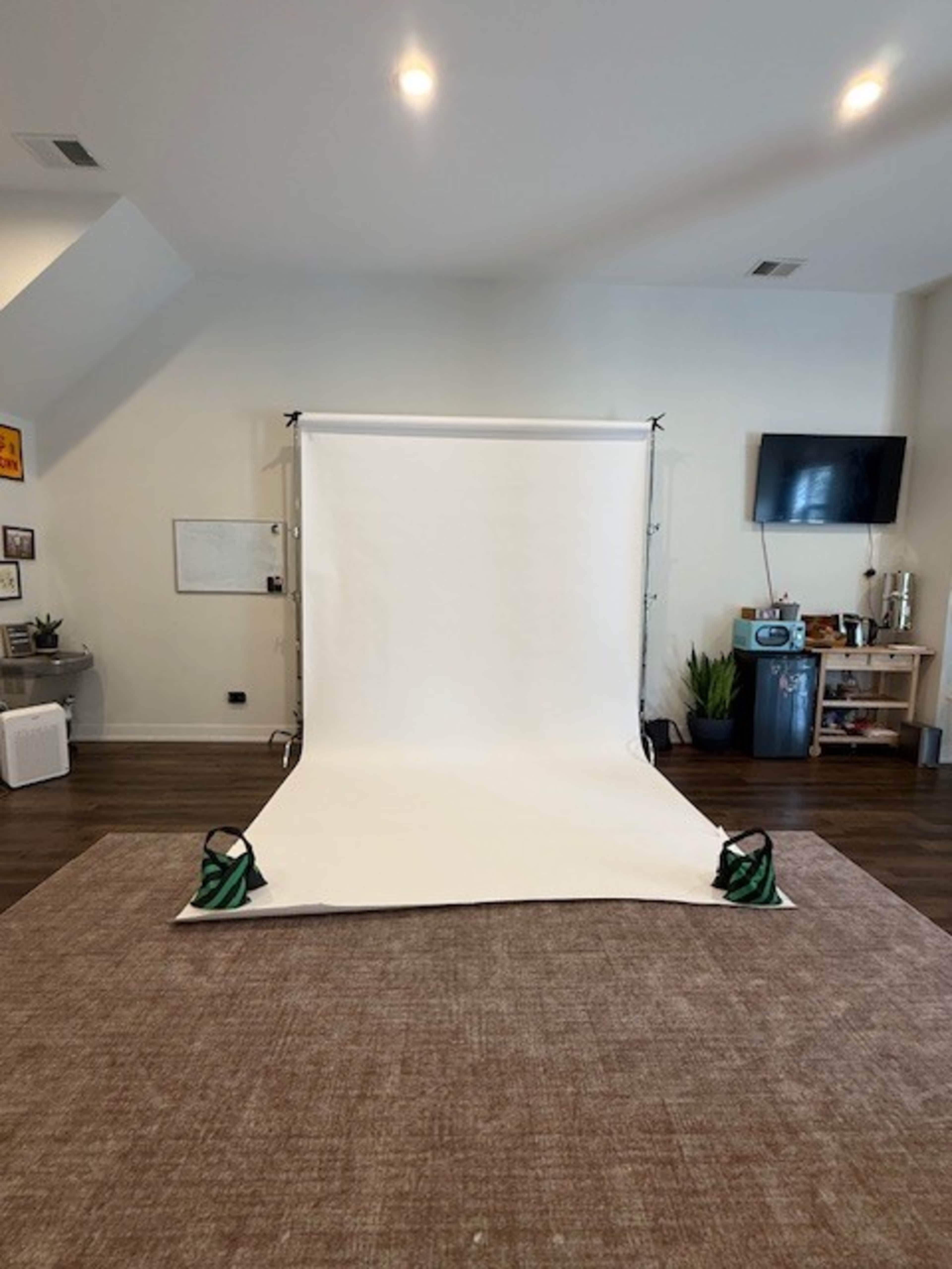 The image shows a photography backdrop setup in a spacious room with a white backdrop, a television, and some furniture along the walls.