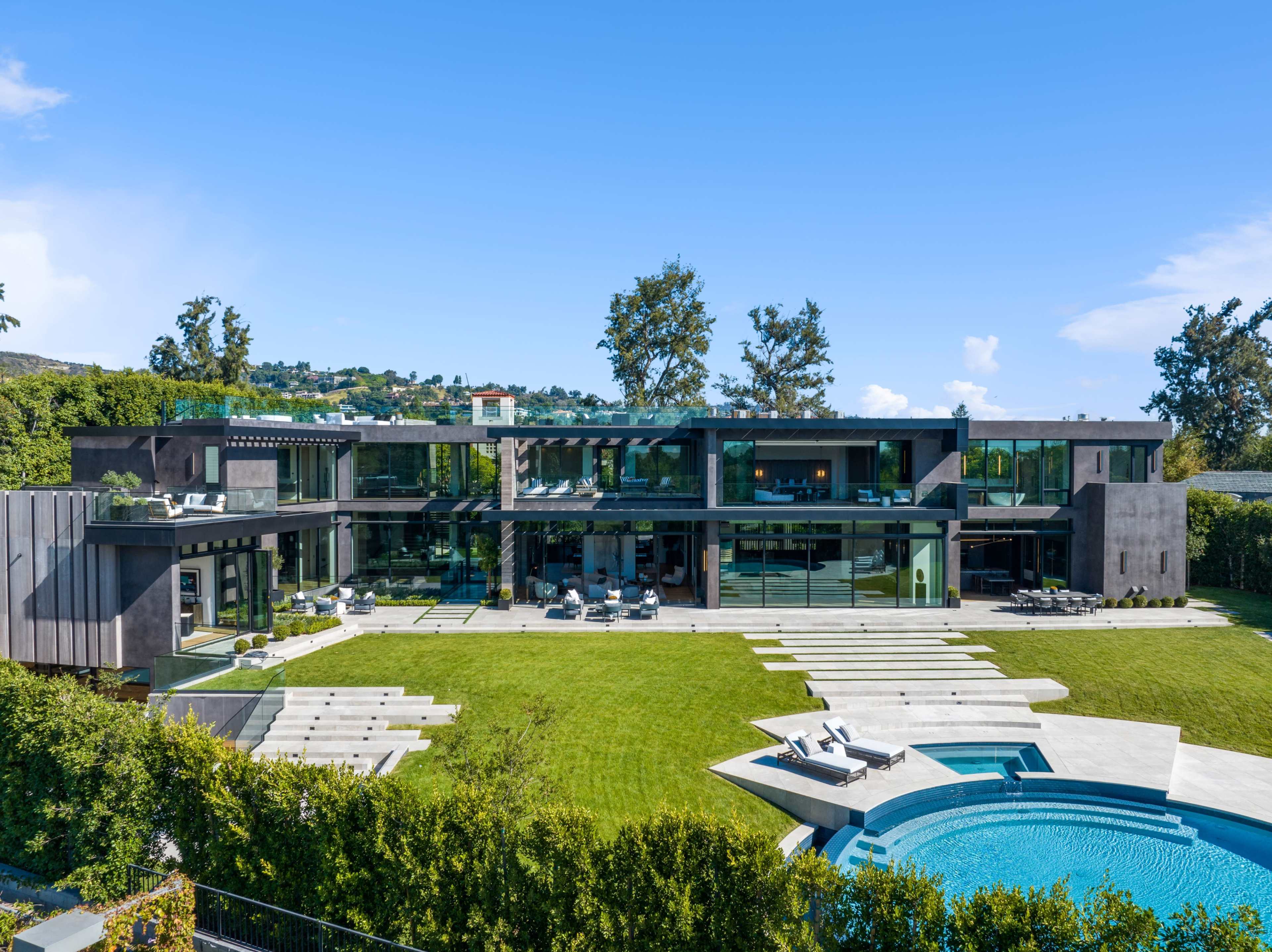 A modern two-story house with large glass windows and a spacious backyard featuring a pool and landscaped greenery.