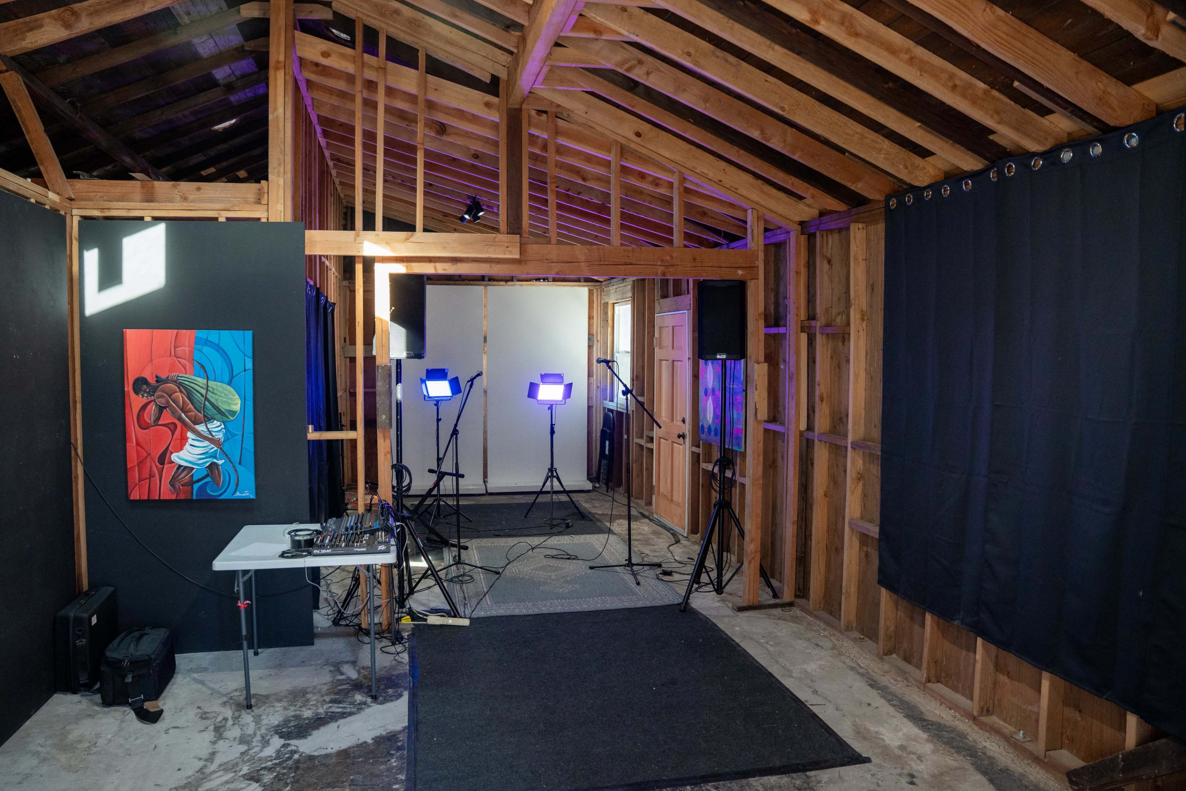 The image shows a partially constructed room with wooden walls, black curtains, and photography lighting setups facing a blank screen.