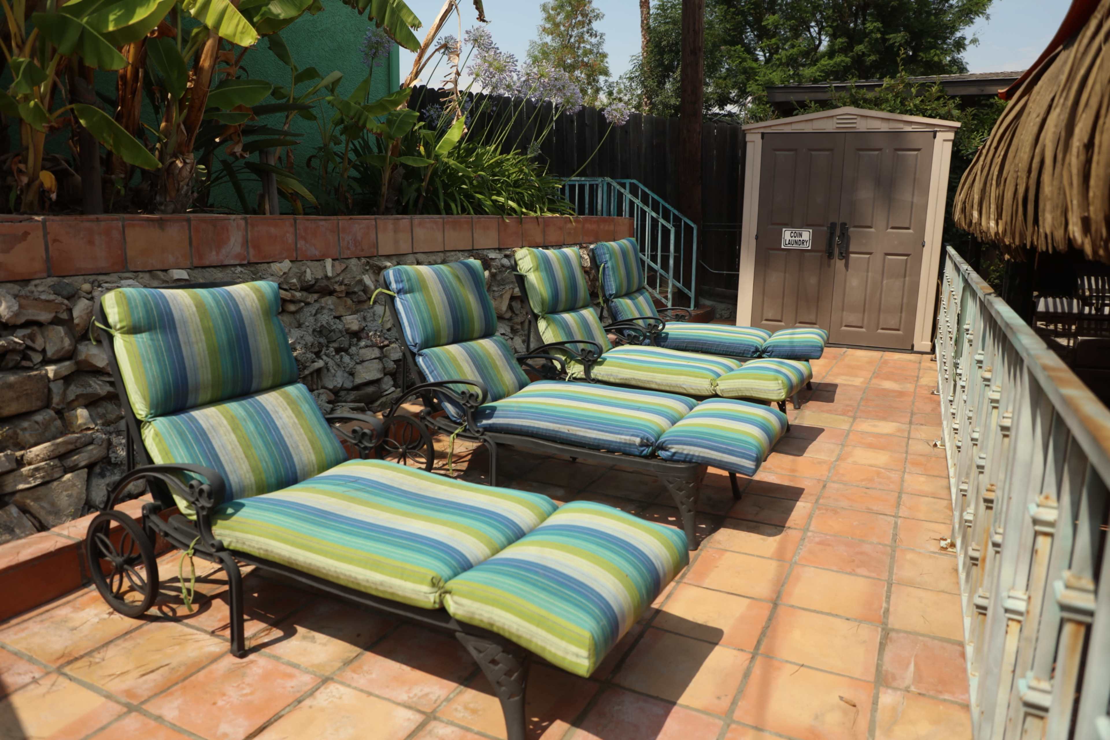 Four striped lounge chairs arranged in a patio area next to a stone wall and a storage shed.