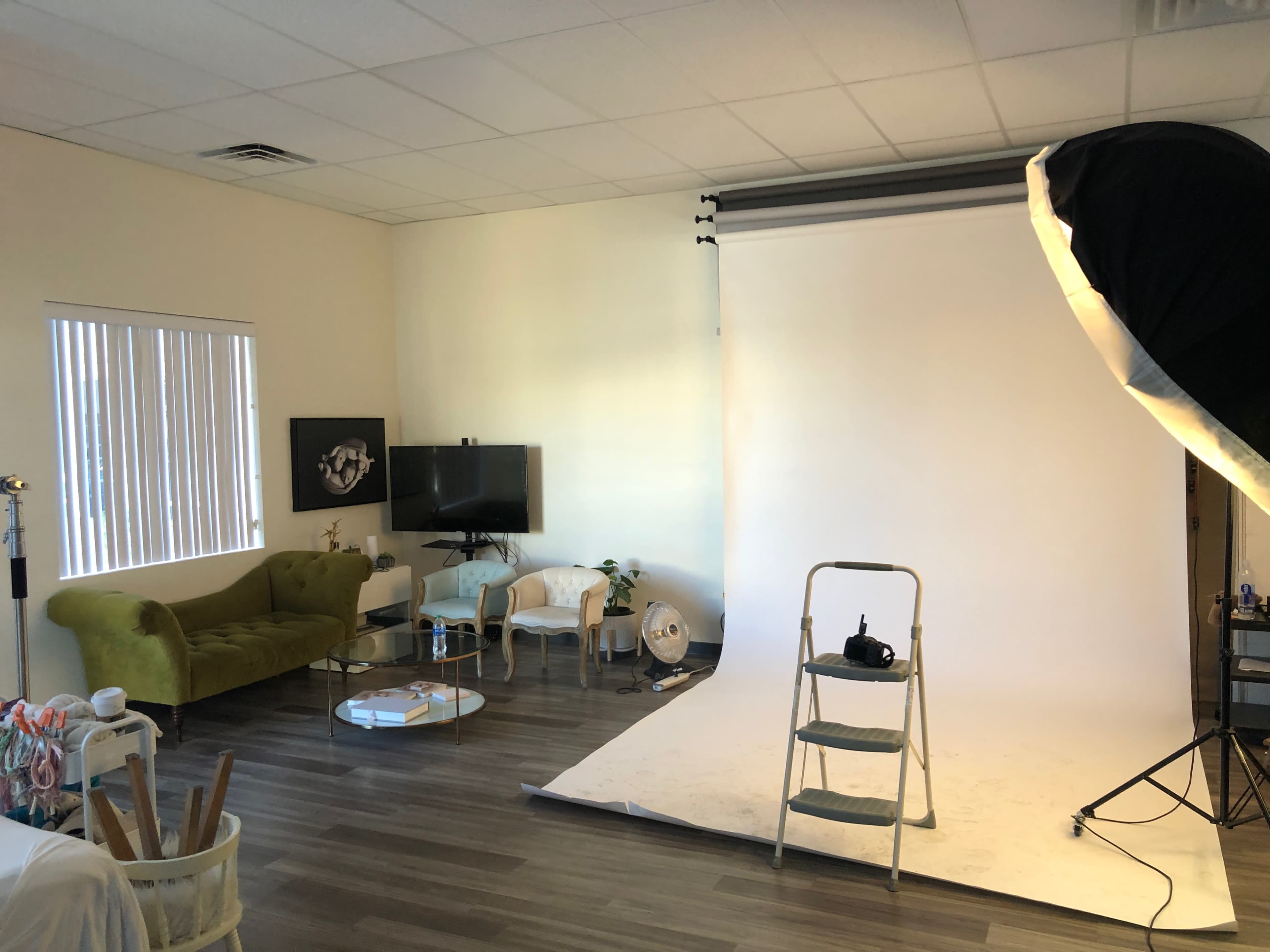 A photography studio with a green sofa, a television, and a backdrop setup featuring a step ladder.