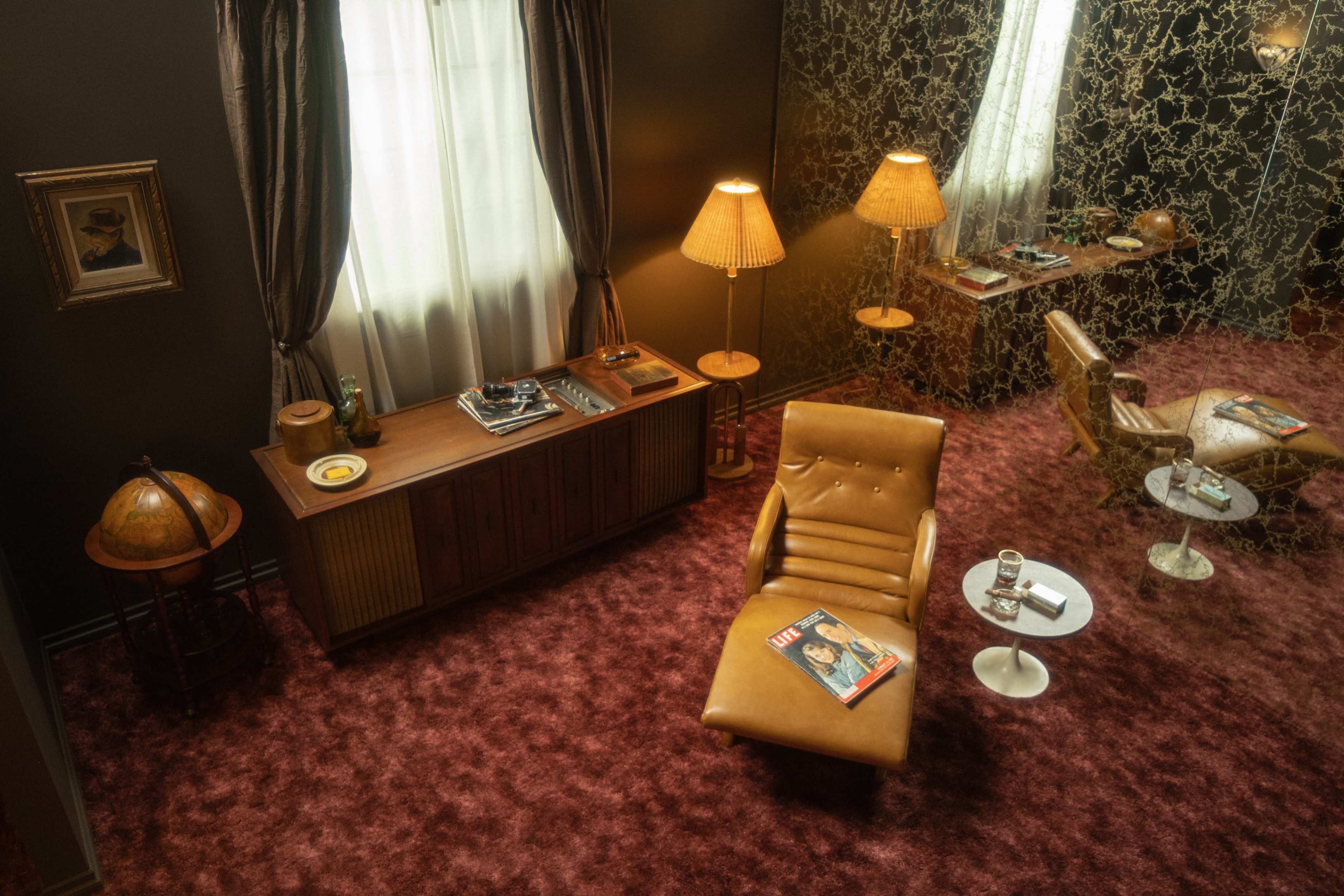 The scene shows a retro-style room with a brown leather chair, a wooden sideboard, and two lamps, surrounded by a patterned wall and a globe.