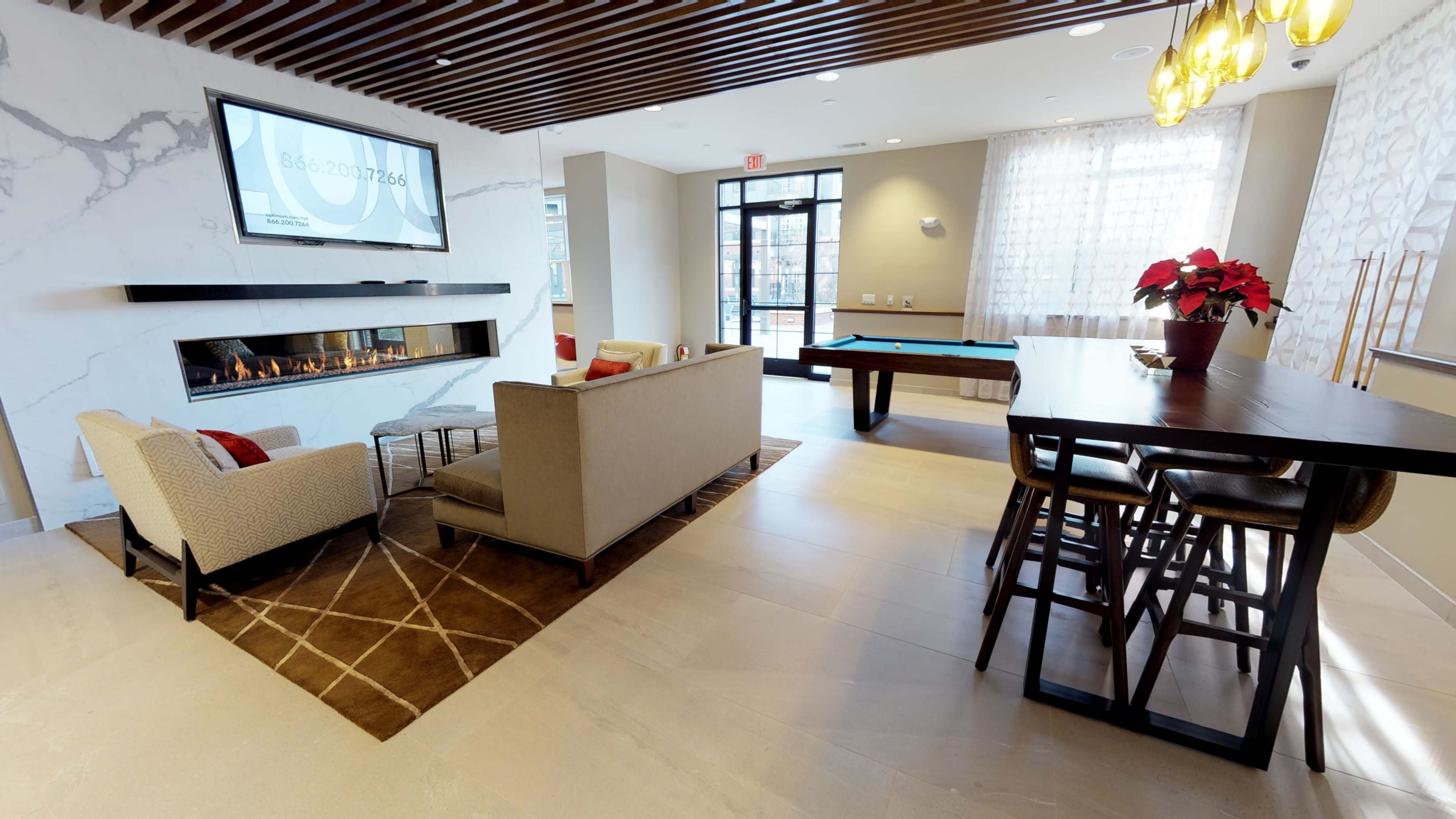 The image shows a modern lounge area with a fireplace, comfortable seating, a pool table, and large windows providing natural light.