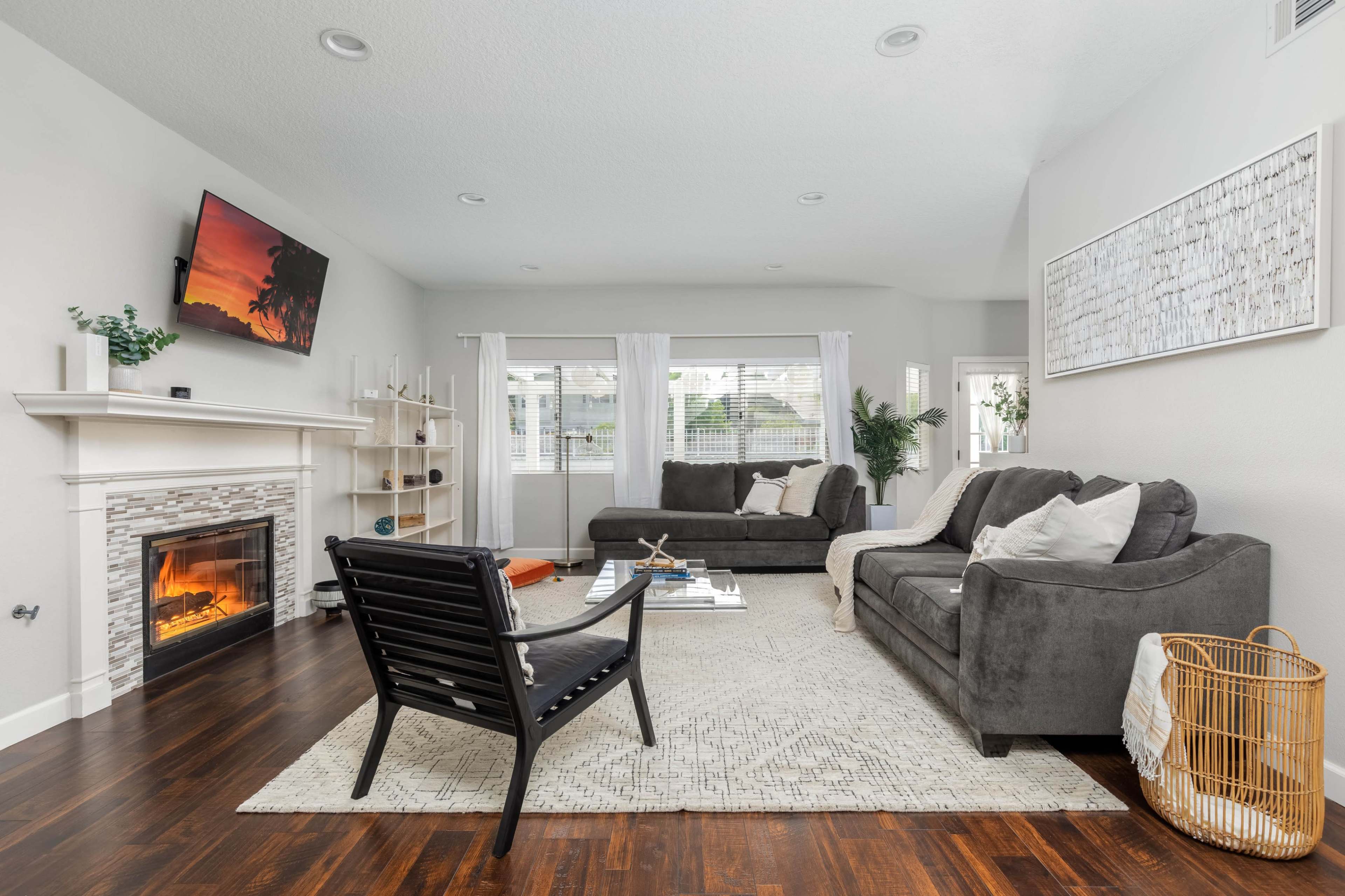 The image shows a modern living room featuring a fireplace, two sofas, a coffee table, and a large window with natural light.