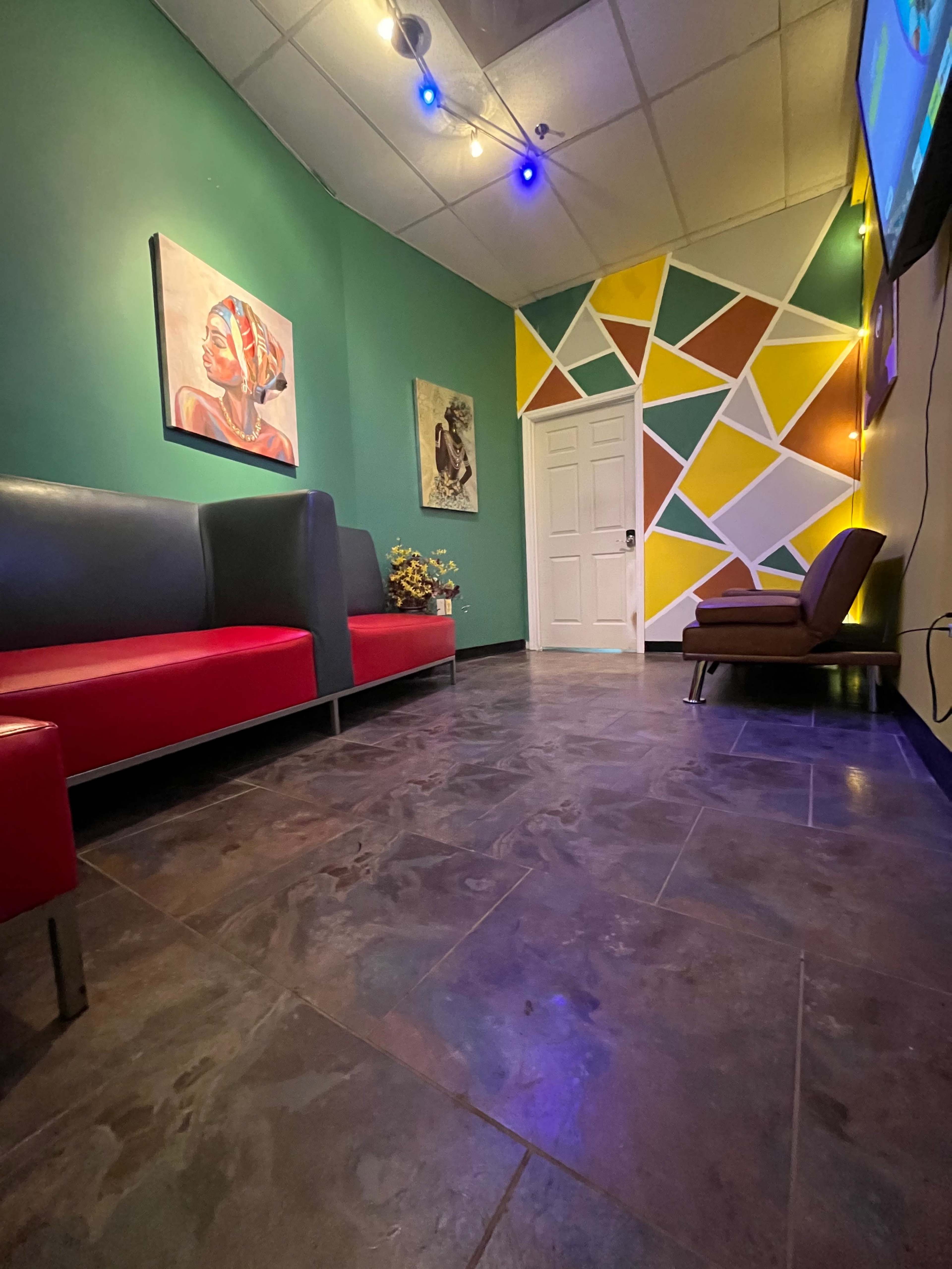 The image shows a brightly colored waiting area with red and gray seating, artwork on the walls, and a door leading to another room.
