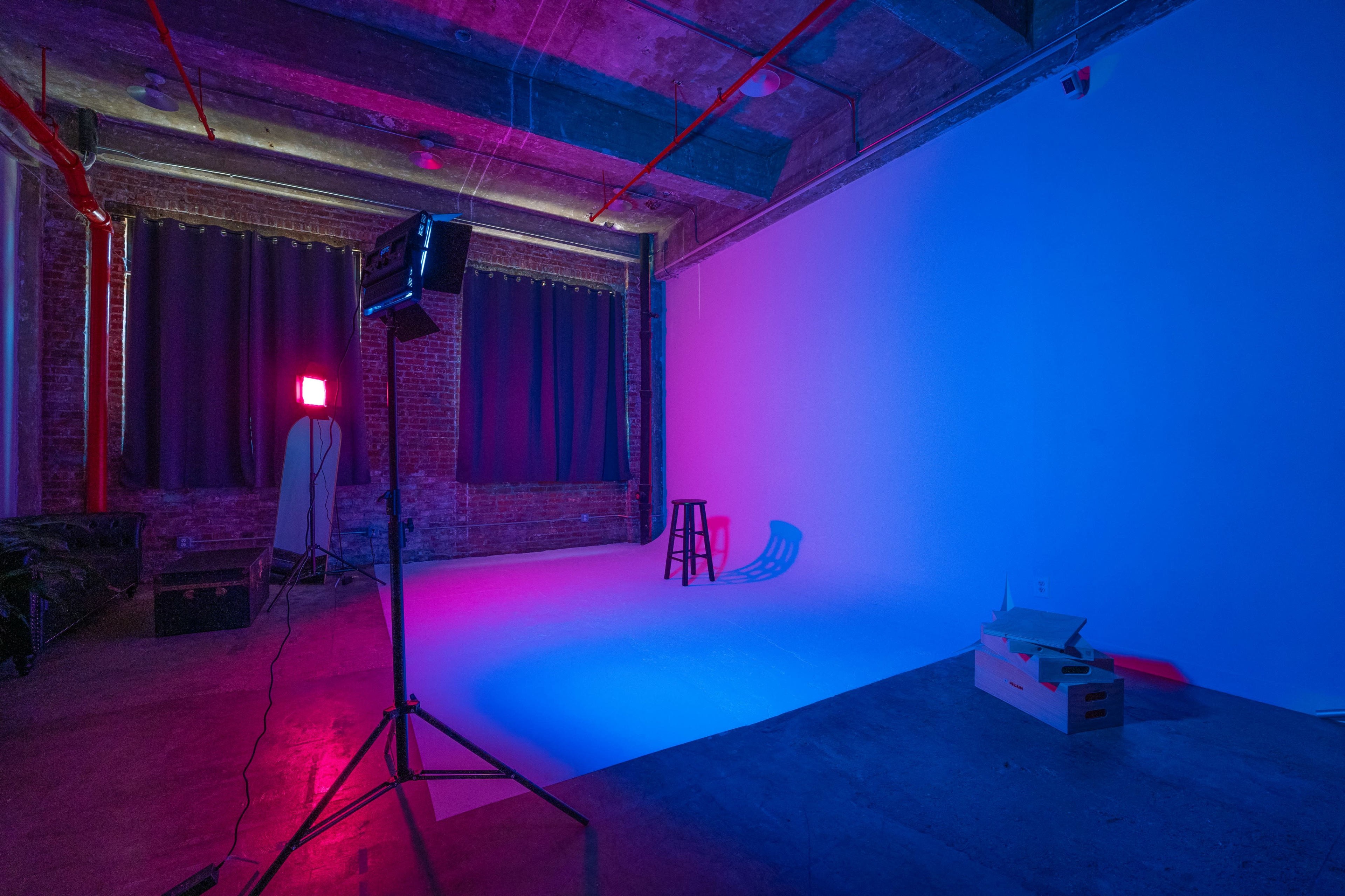 A photography studio features a bright backdrop with contrasting color lights, a stool, and various equipment scattered across the floor.