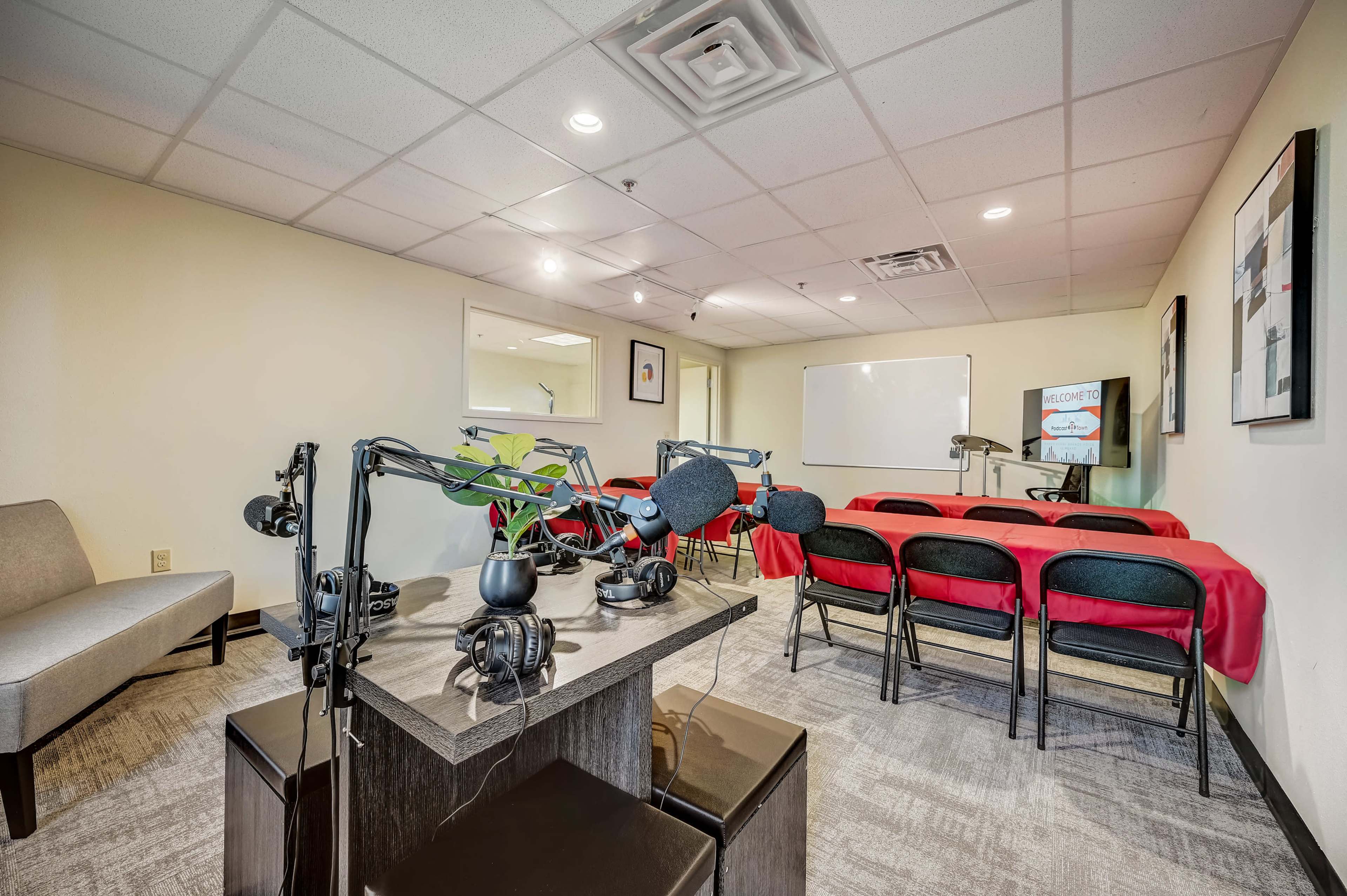 A small conference room equipped with a black table and chairs, a whiteboard, and a podcasting setup featuring microphones and headphones.