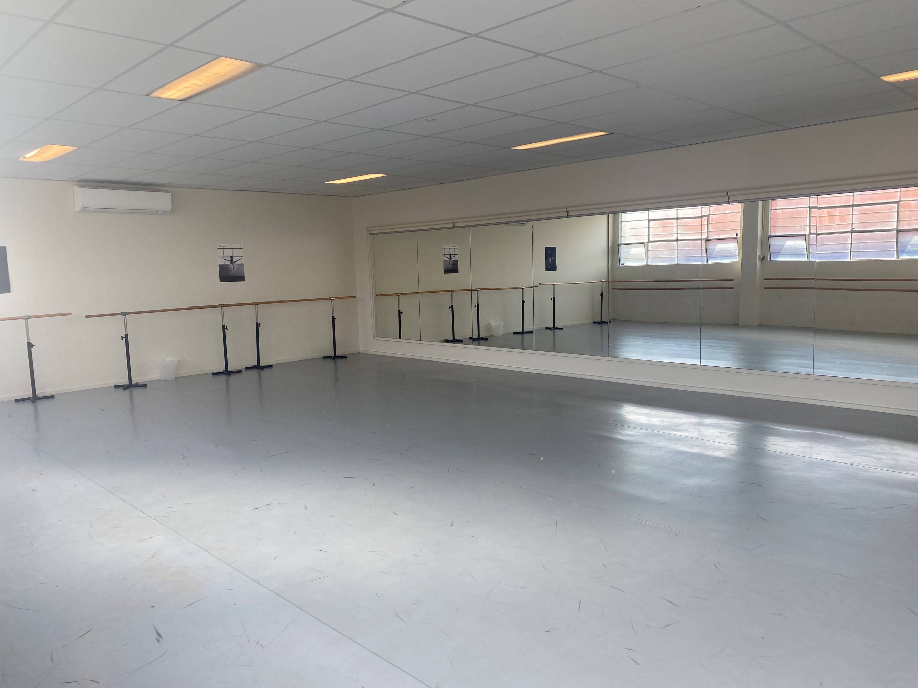 A clean dance studio with a thin ballet bar along one wall and mirrors reflecting the empty space.