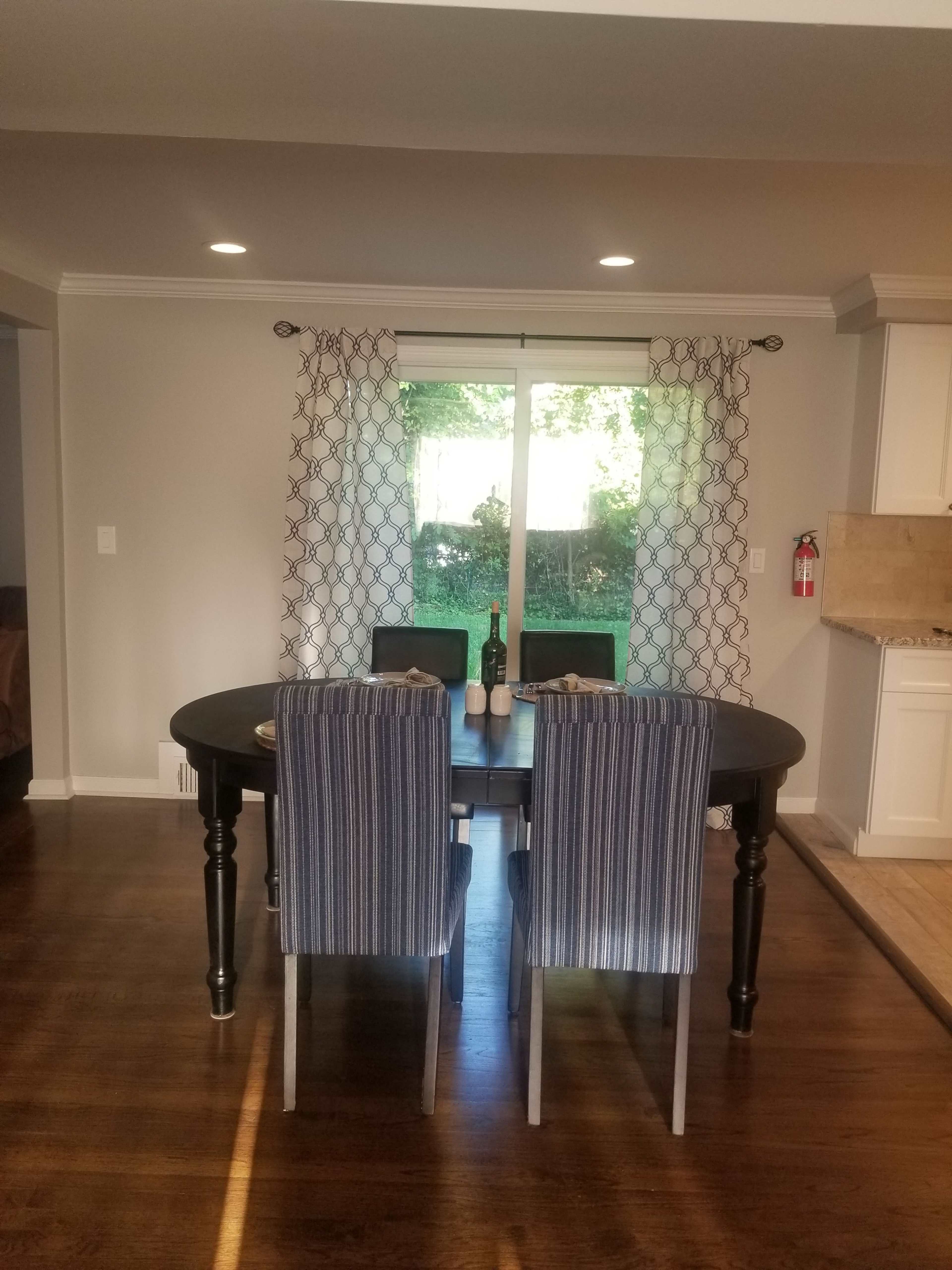 A dining area with a round table set for two and a view of a green backyard through a glass door.
