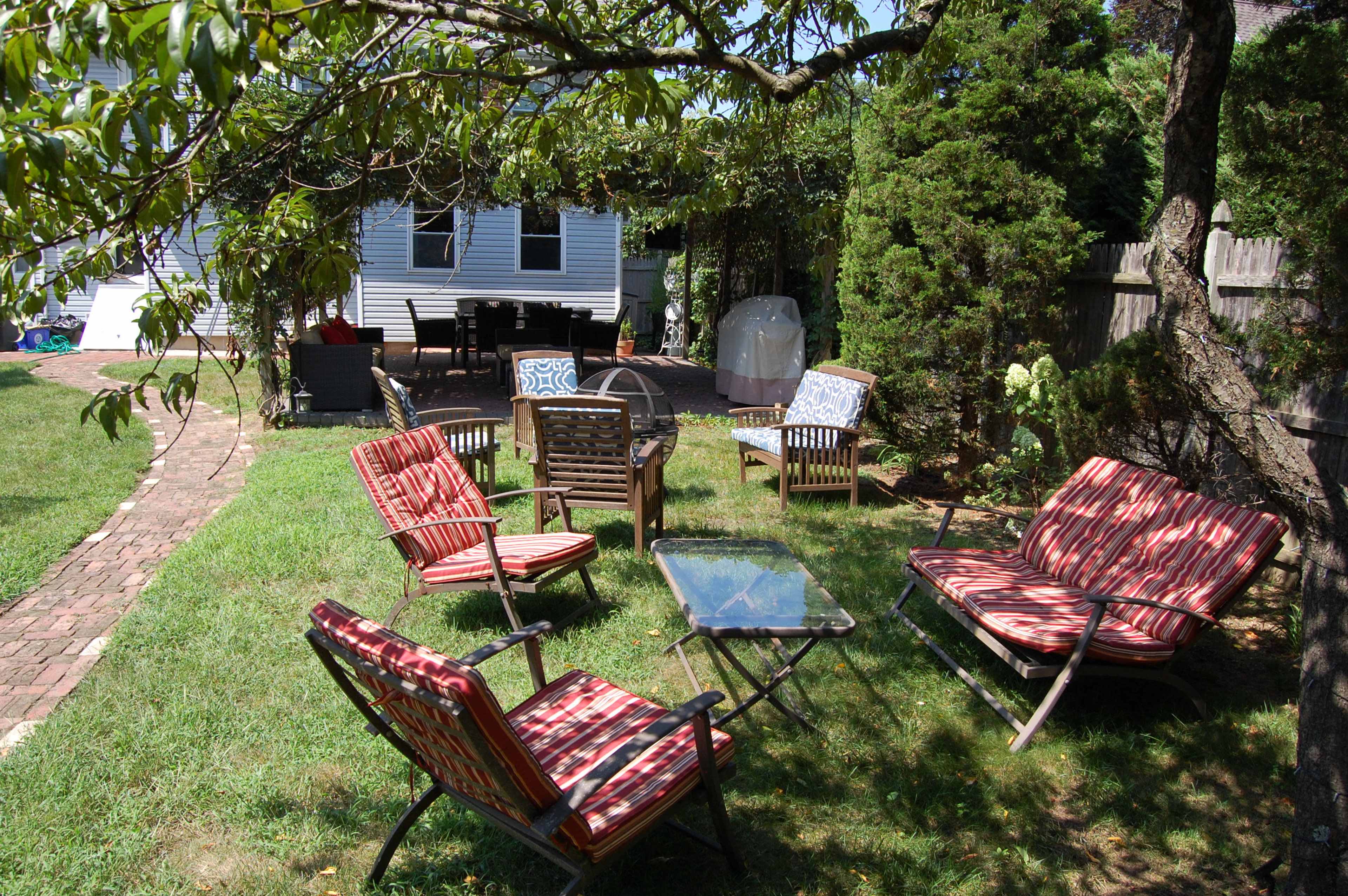 A patio area with several striped lounge chairs and a glass table is surrounded by grass and trees.