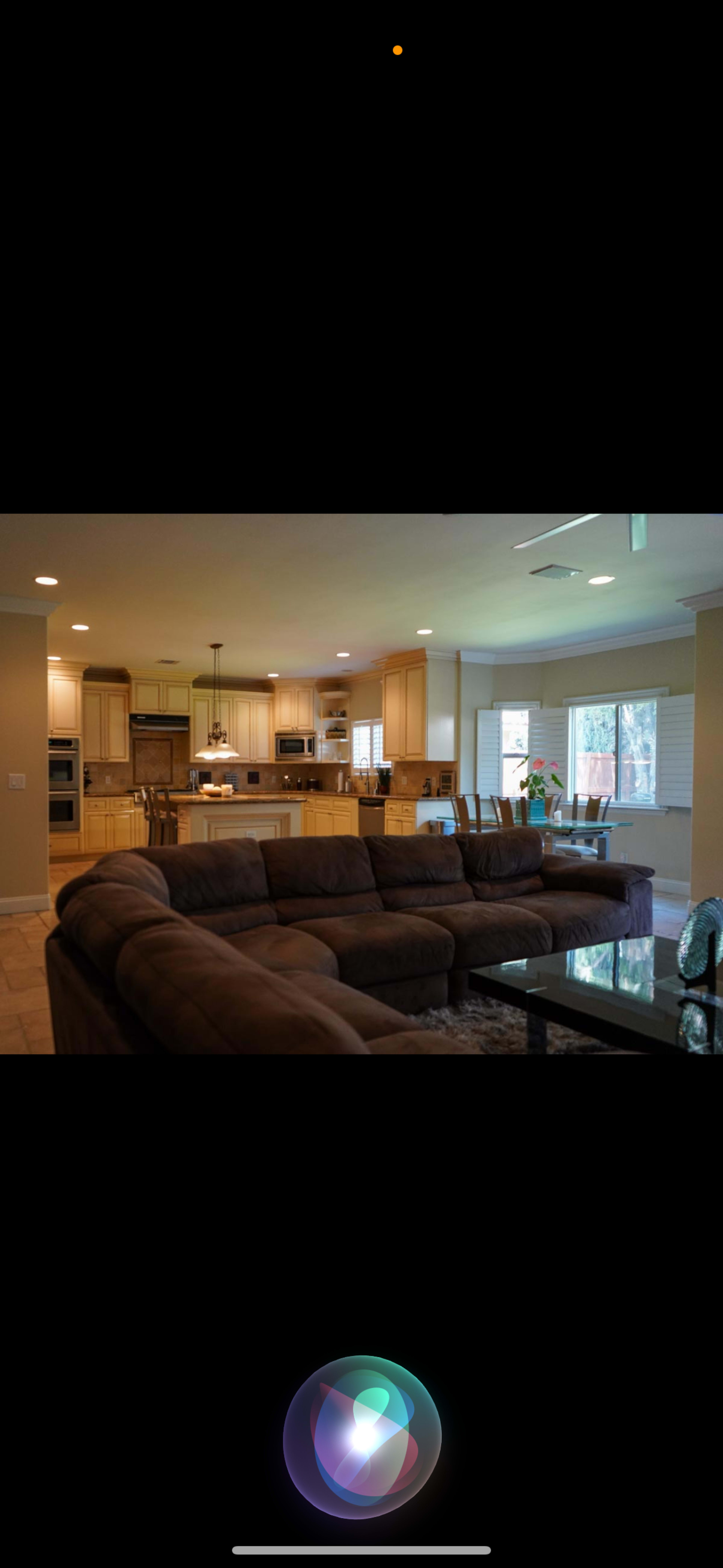 A spacious kitchen and living area with brown couches, a coffee table, and light wood cabinetry.