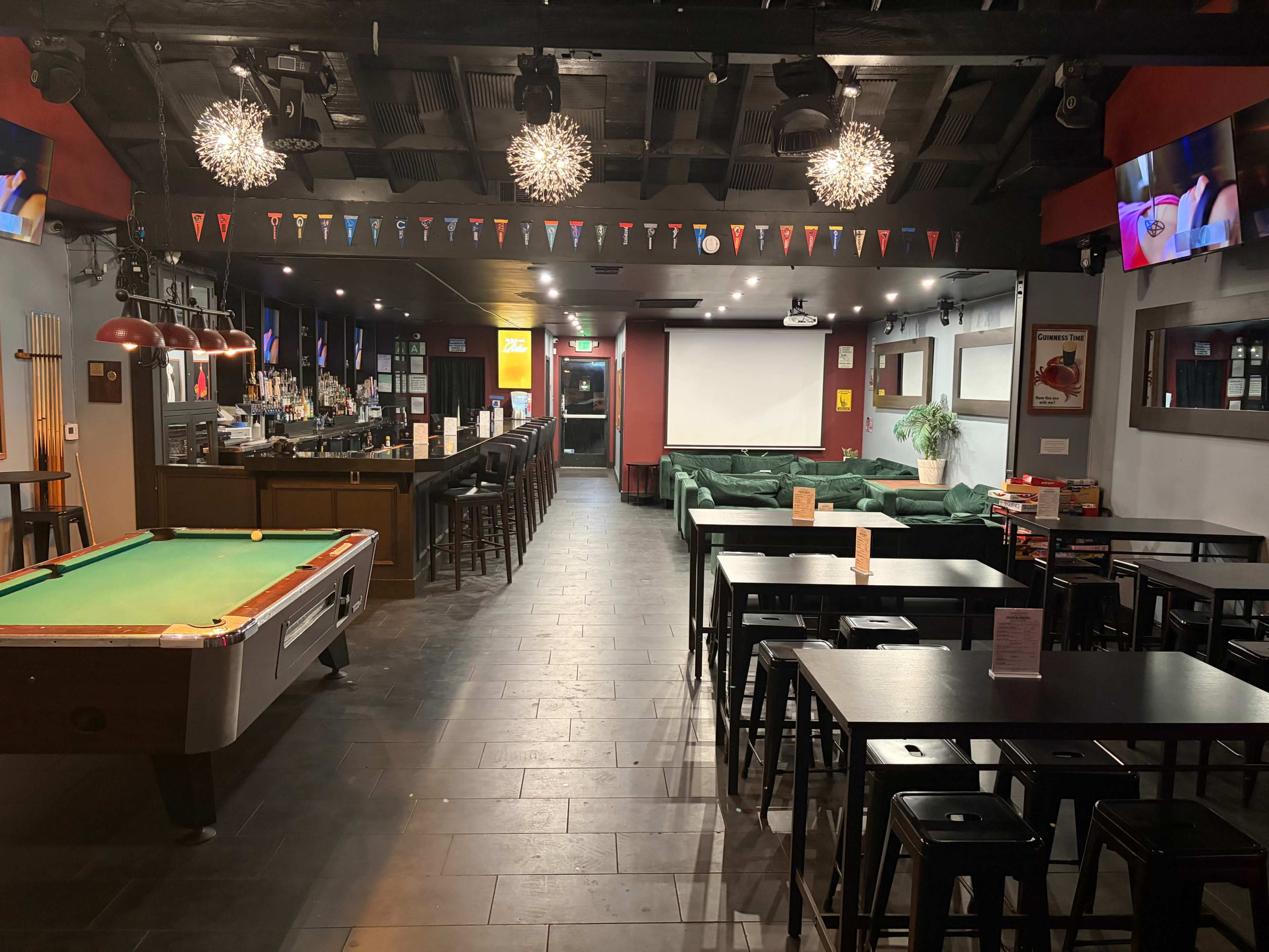 The image shows the interior of a bar or lounge with a pool table on the left, seating areas, a bar counter in the background, and decorative lights overhead.