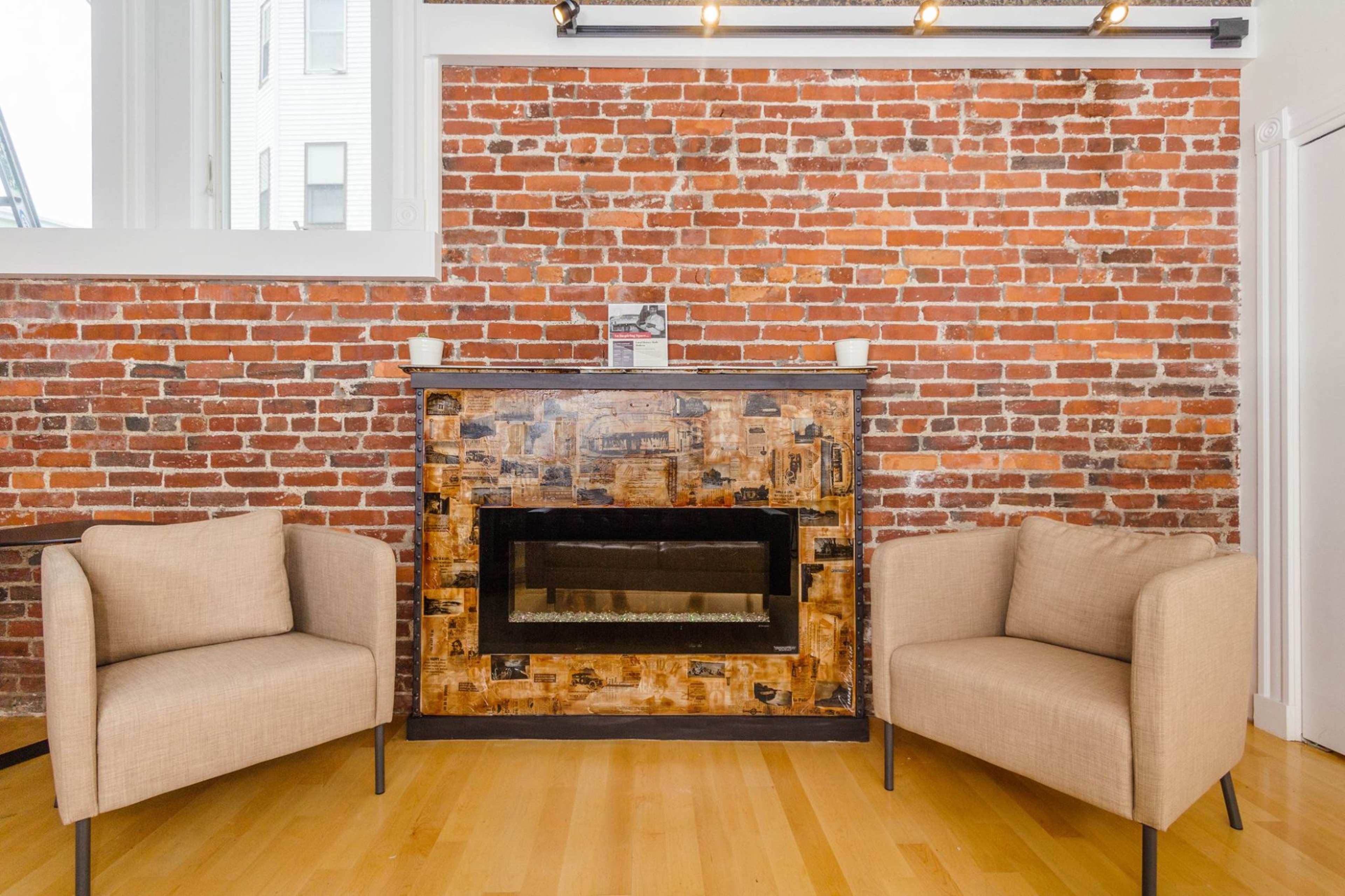 A cozy room with a brick wall, two light-colored chairs, and a decorative fireplace.