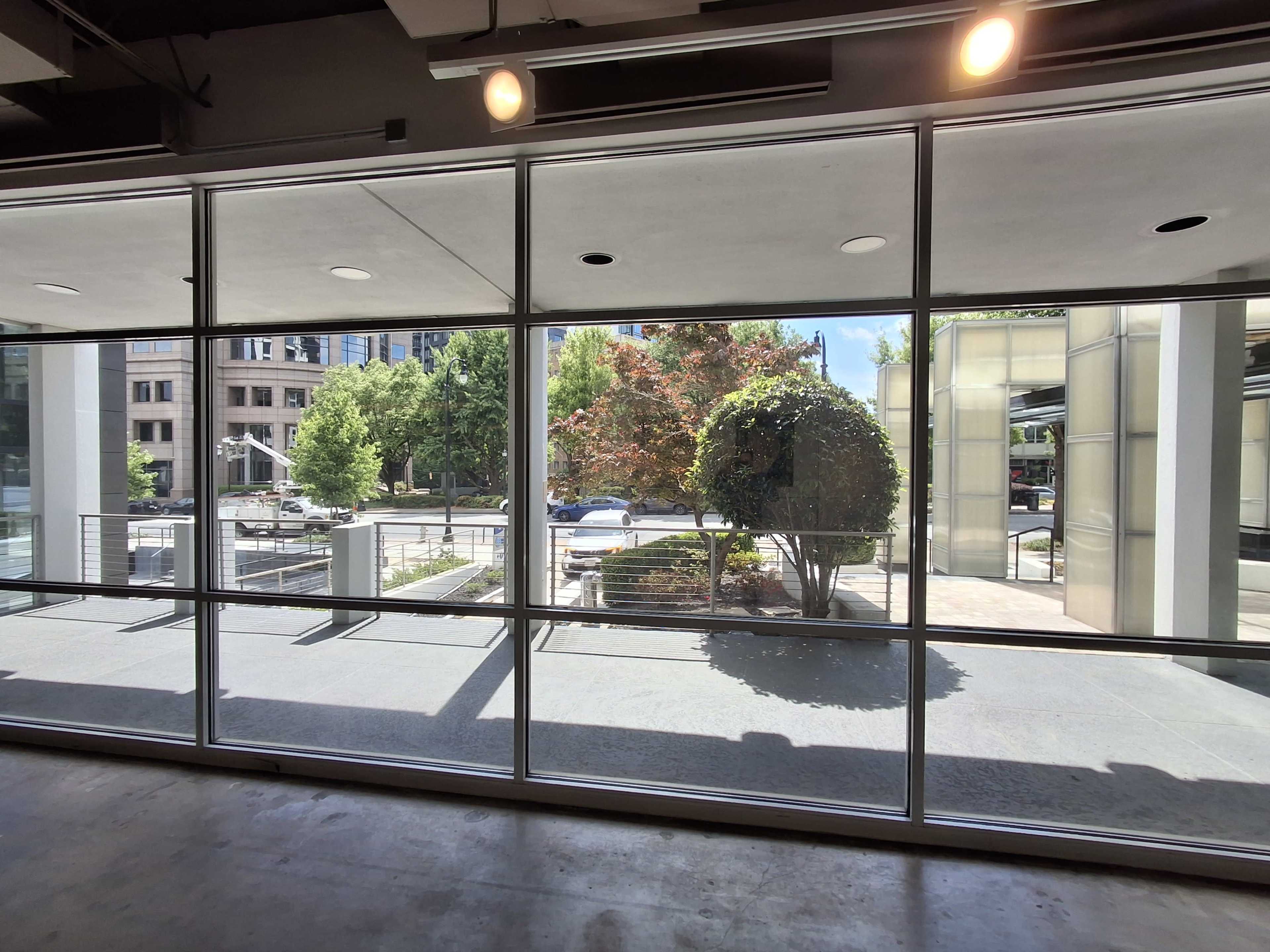 The image shows a large window with a view of a landscaped area featuring trees and parked cars outside a building.