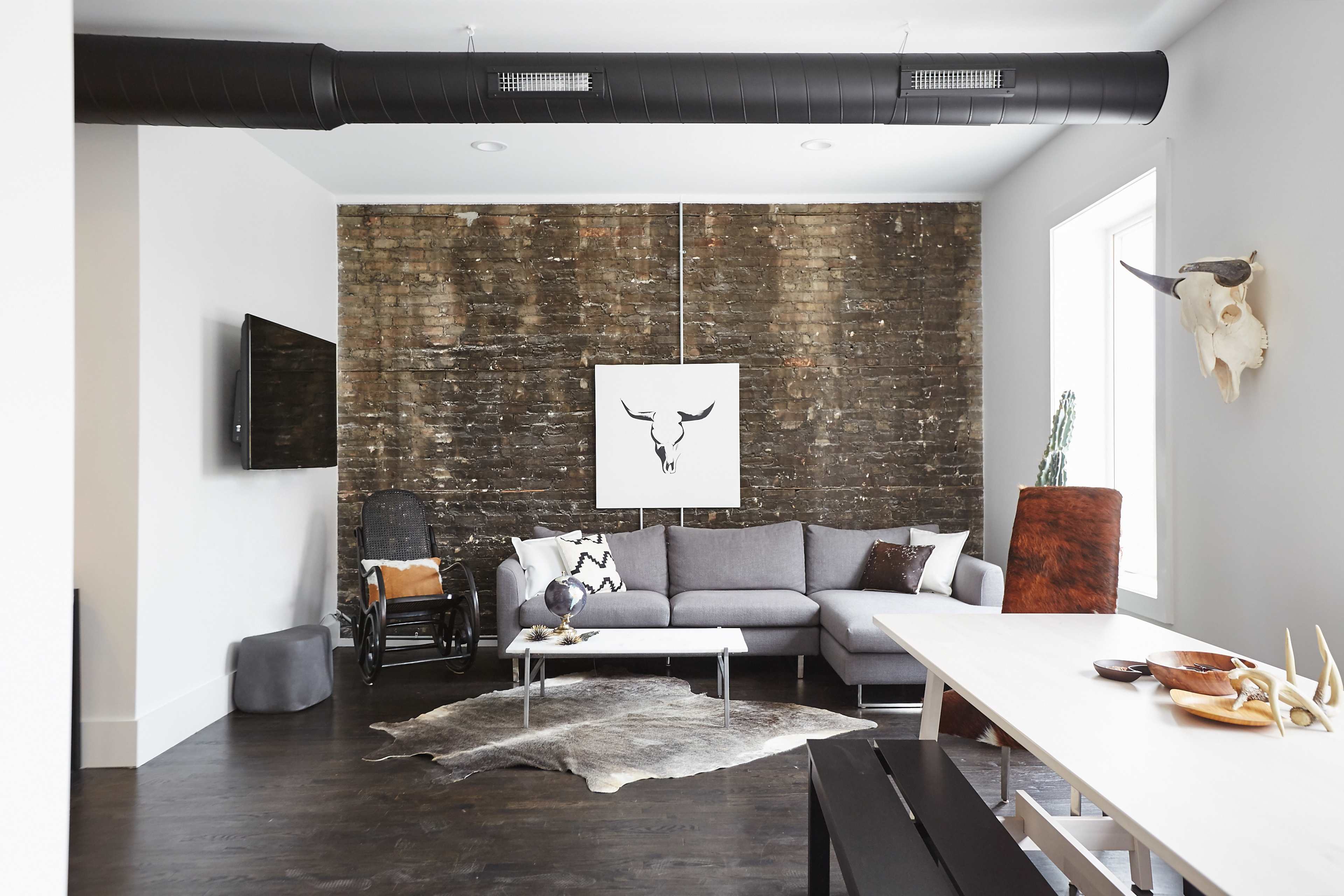 The living room features a gray sectional sofa, a wooden dining table, and a rustic accent wall with a large bull print.