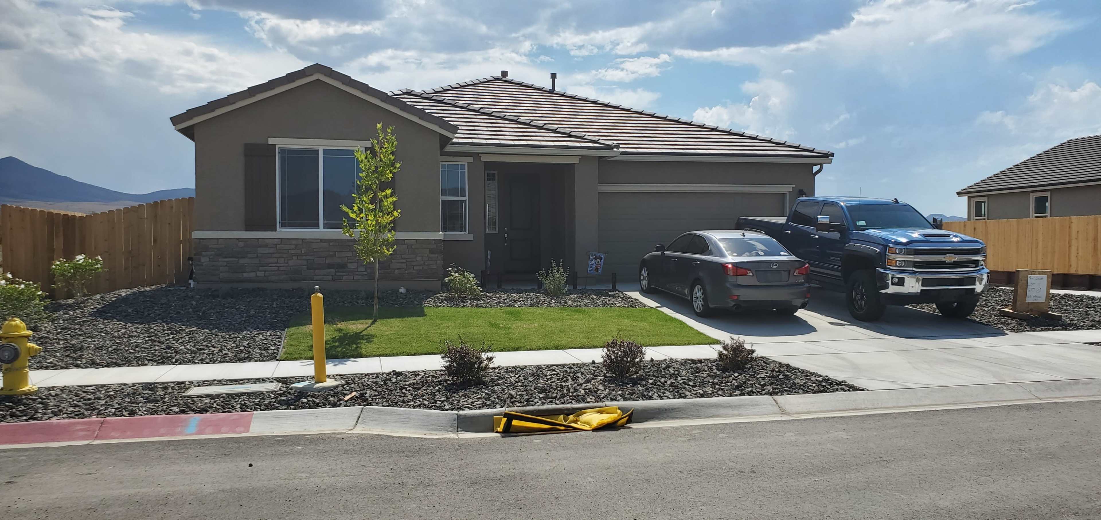 A modern single-story house with a stone-accented exterior, two vehicles parked in the driveway, and landscaped front yard features.