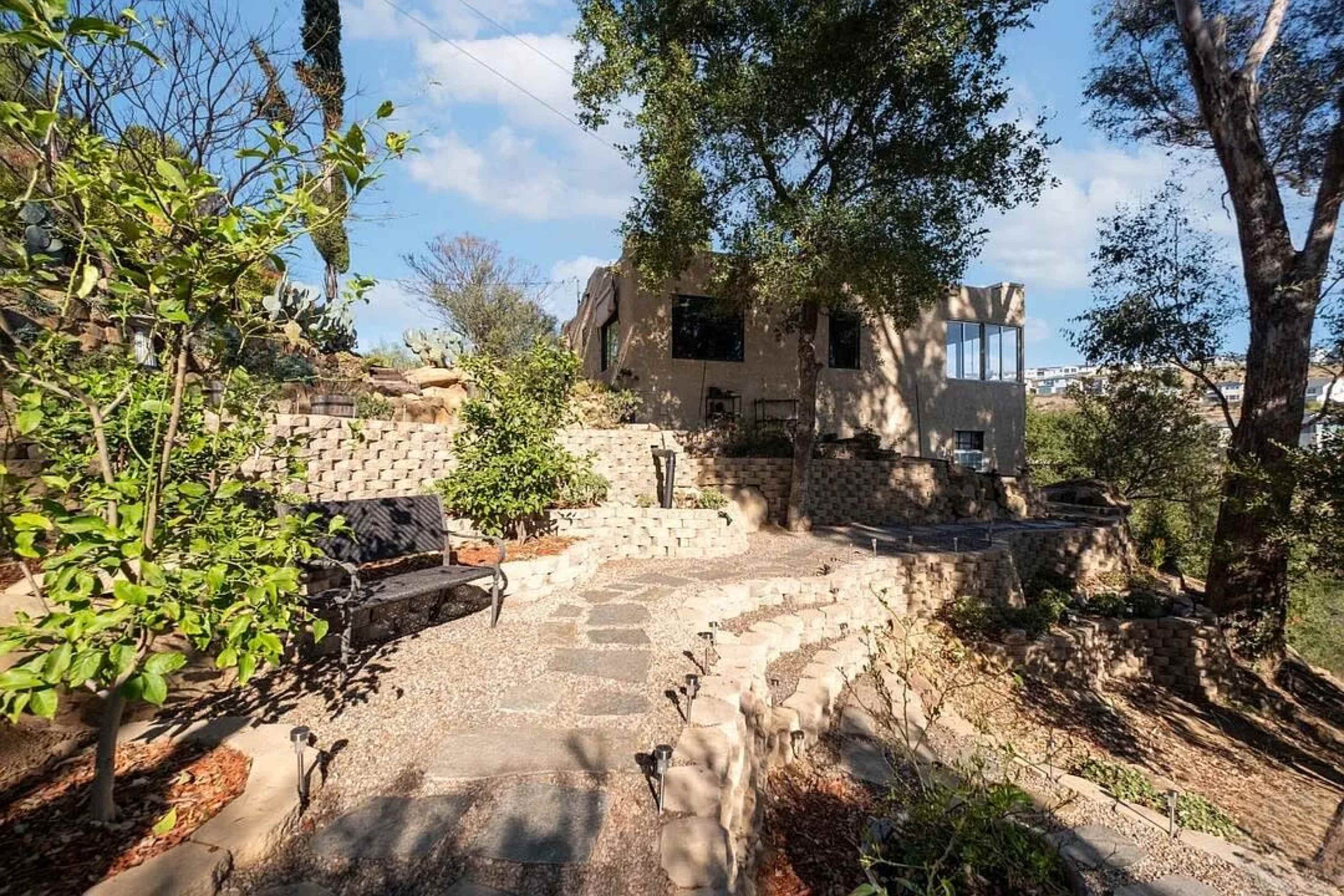 The image shows a stone pathway winding through a landscaped garden with a modern house in the background.