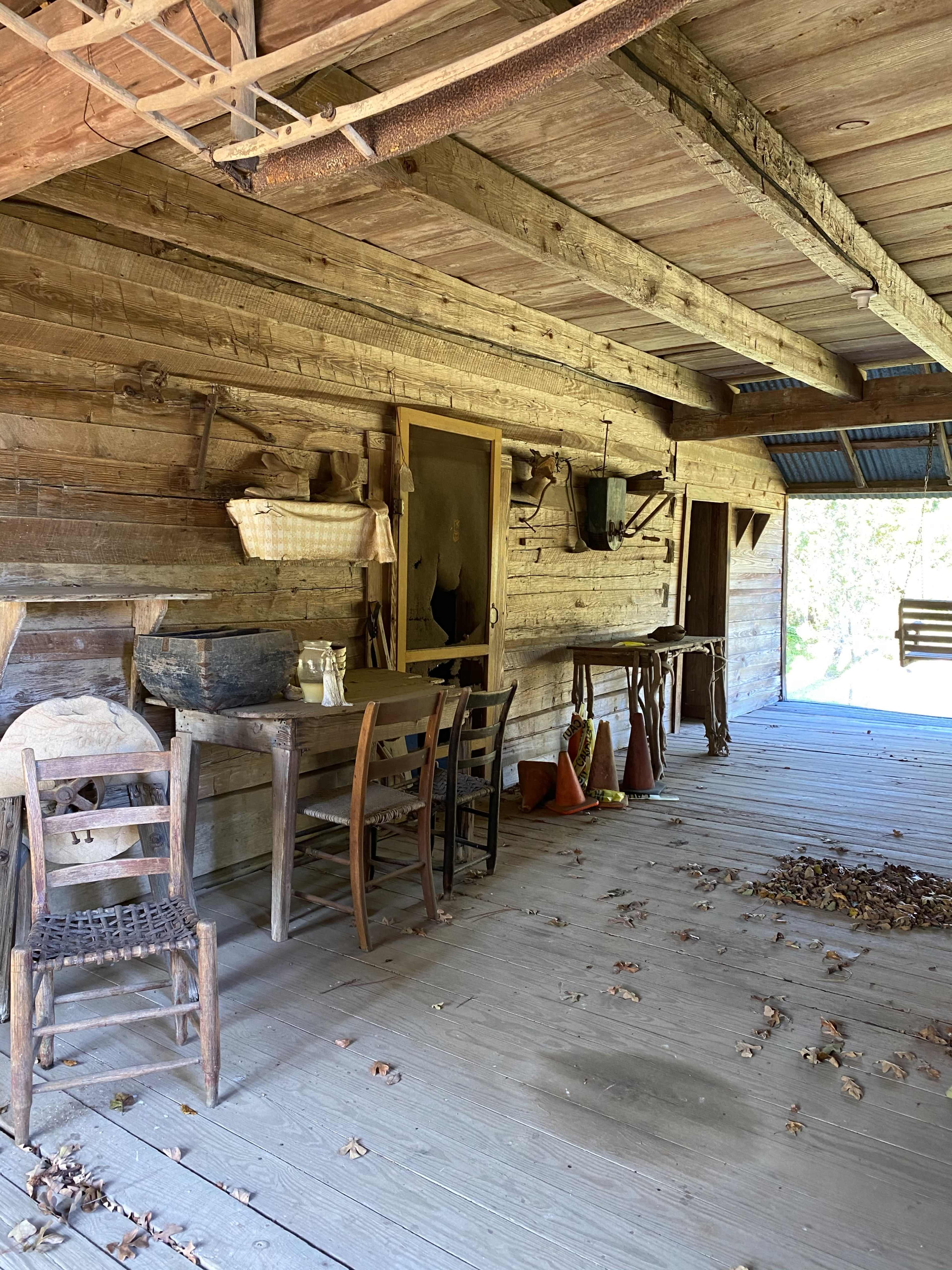 A wooden porch with tables, chairs, and various tools against a rustic wall.