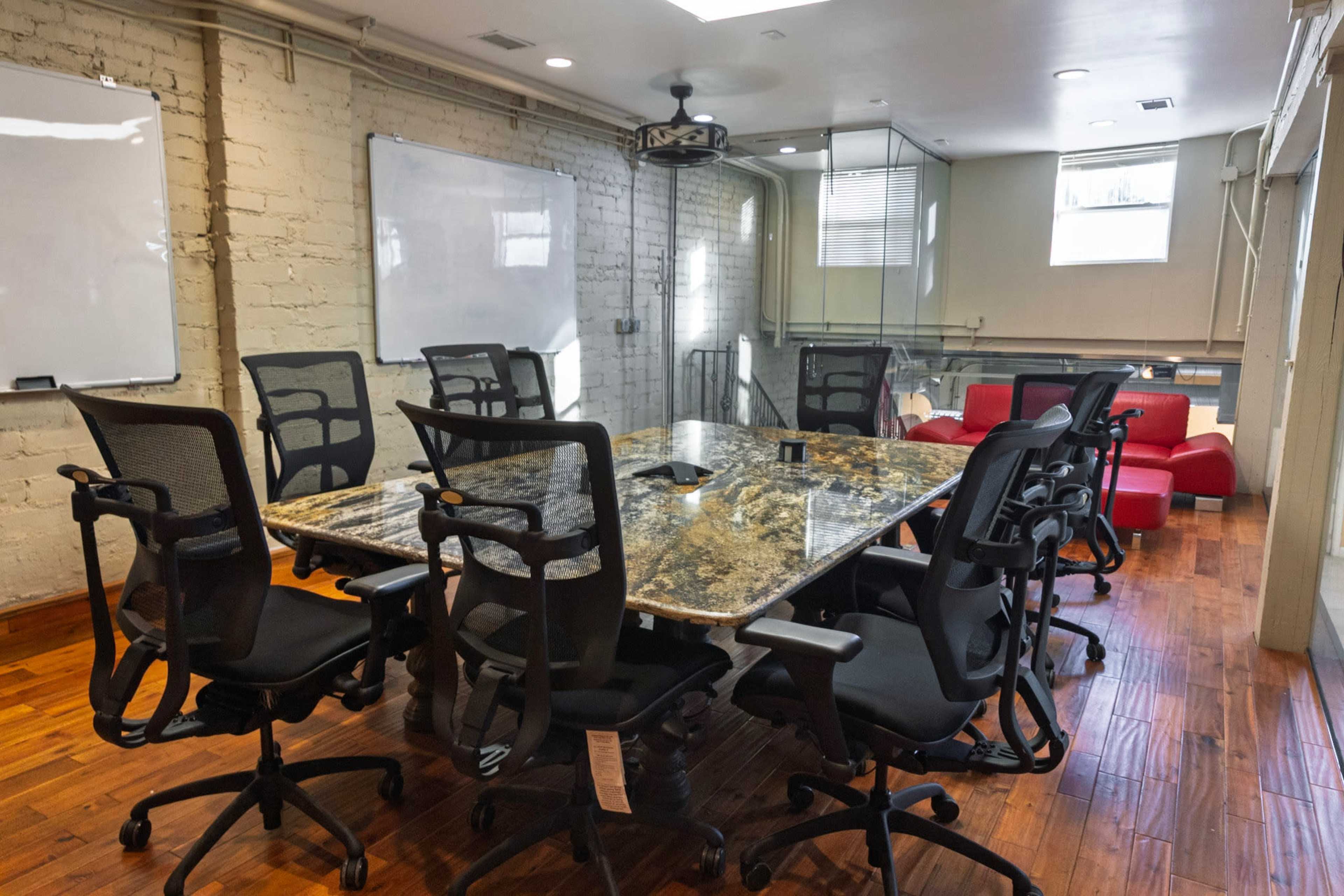 The image shows a modern conference room with a large granite table surrounded by black ergonomic chairs and two whiteboards on opposite walls.
