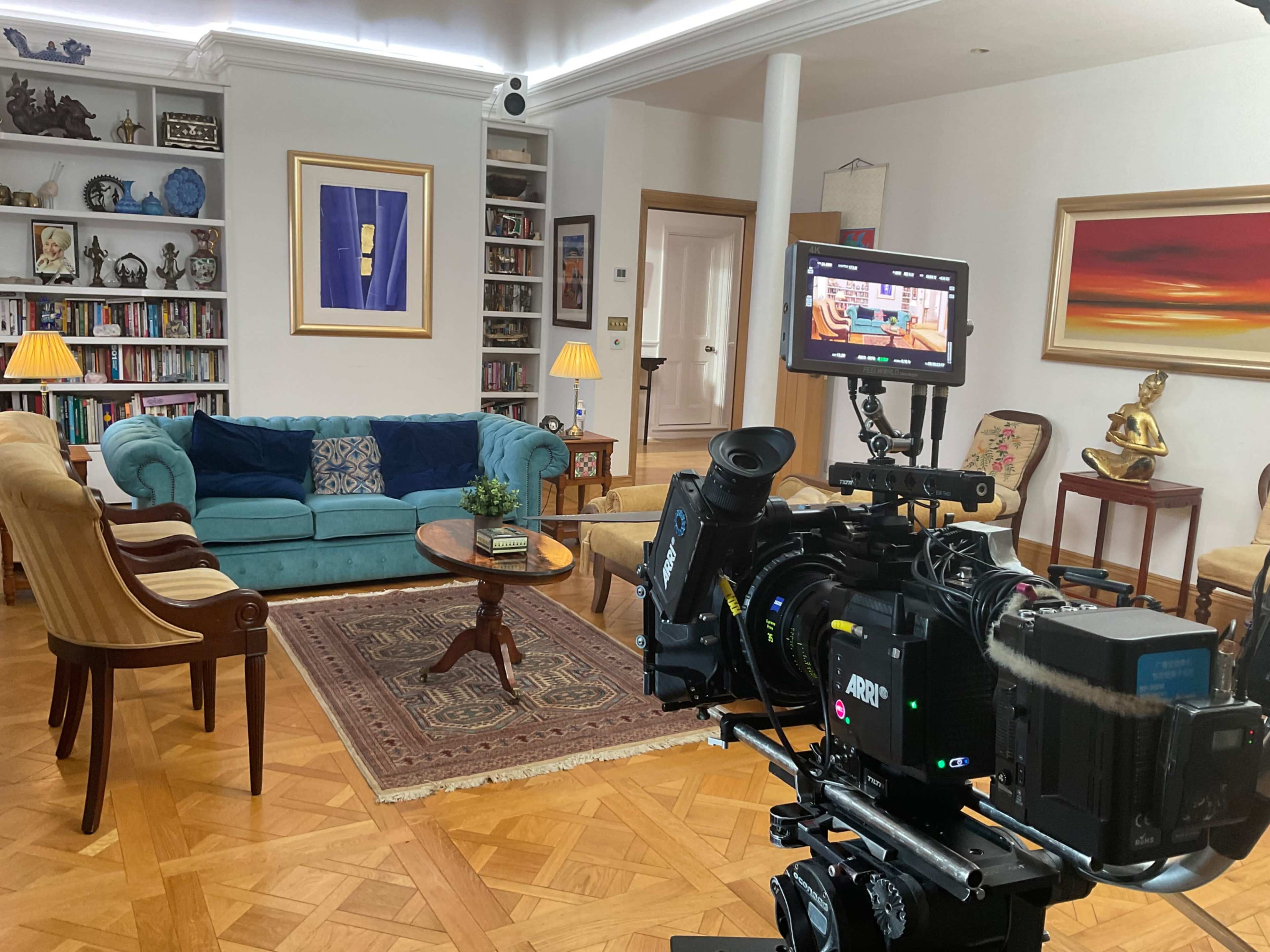 A camera setup is focused on a cozy living room featuring a blue couch, a coffee table, and bookshelves filled with books.